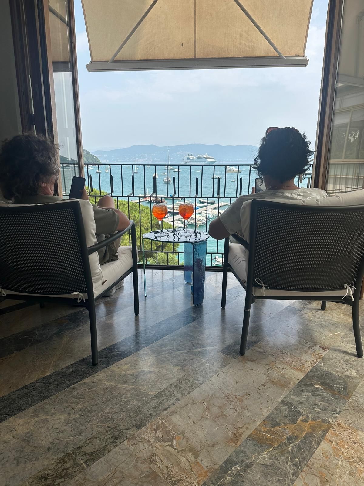 Due persone sedute su un balcone sorseggiano un drink ammirando la vista panoramica sull'oceano.