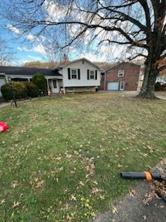 A white, two-story house with a brick garage adjacent, viewed across a grassy yard with fallen leaves under a blue sky.