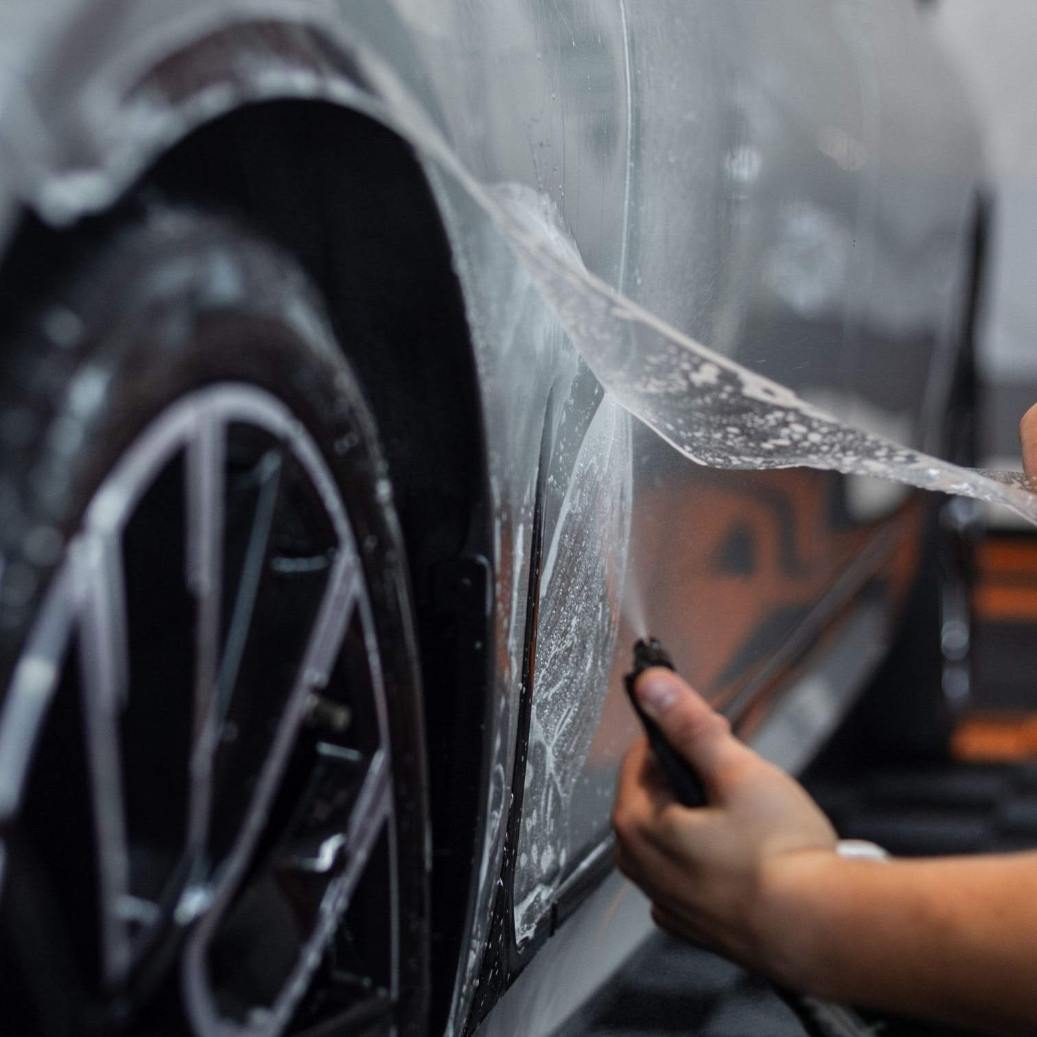 Person peeling protective film from a black car door and wheel during detailing
