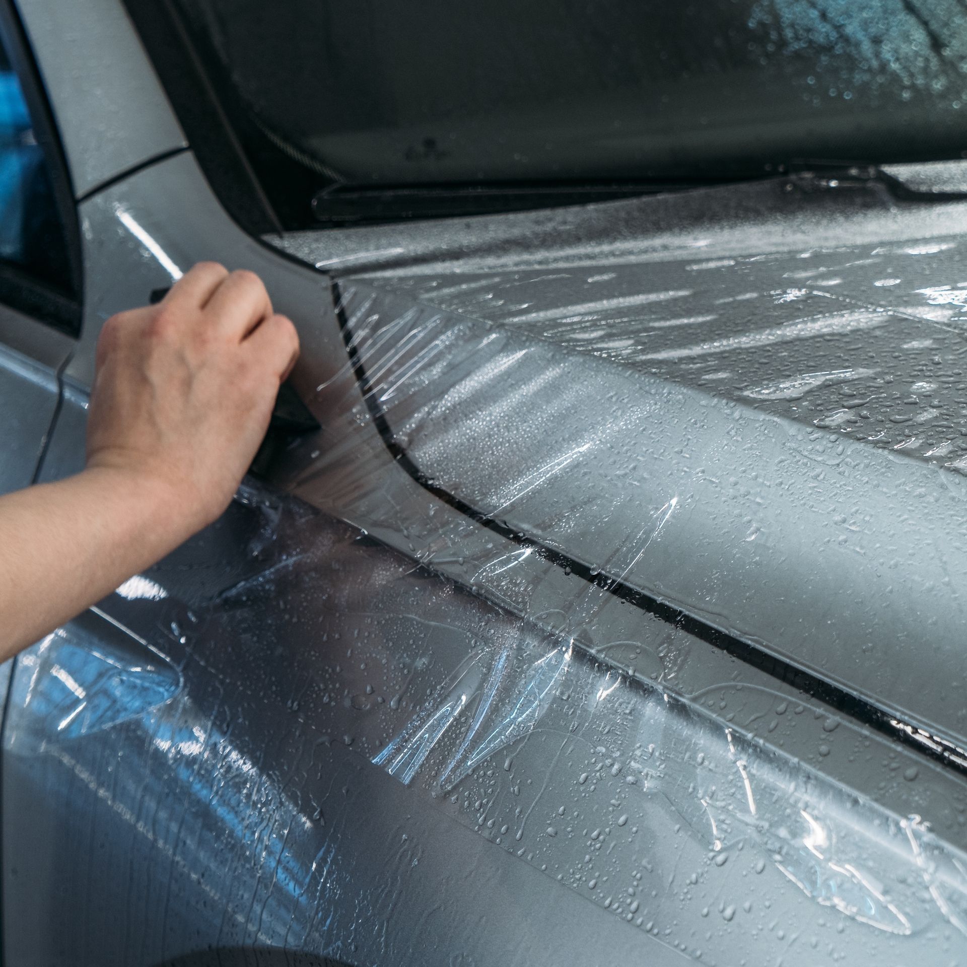 Hand applying protective film to a silver car hood and windshield edge