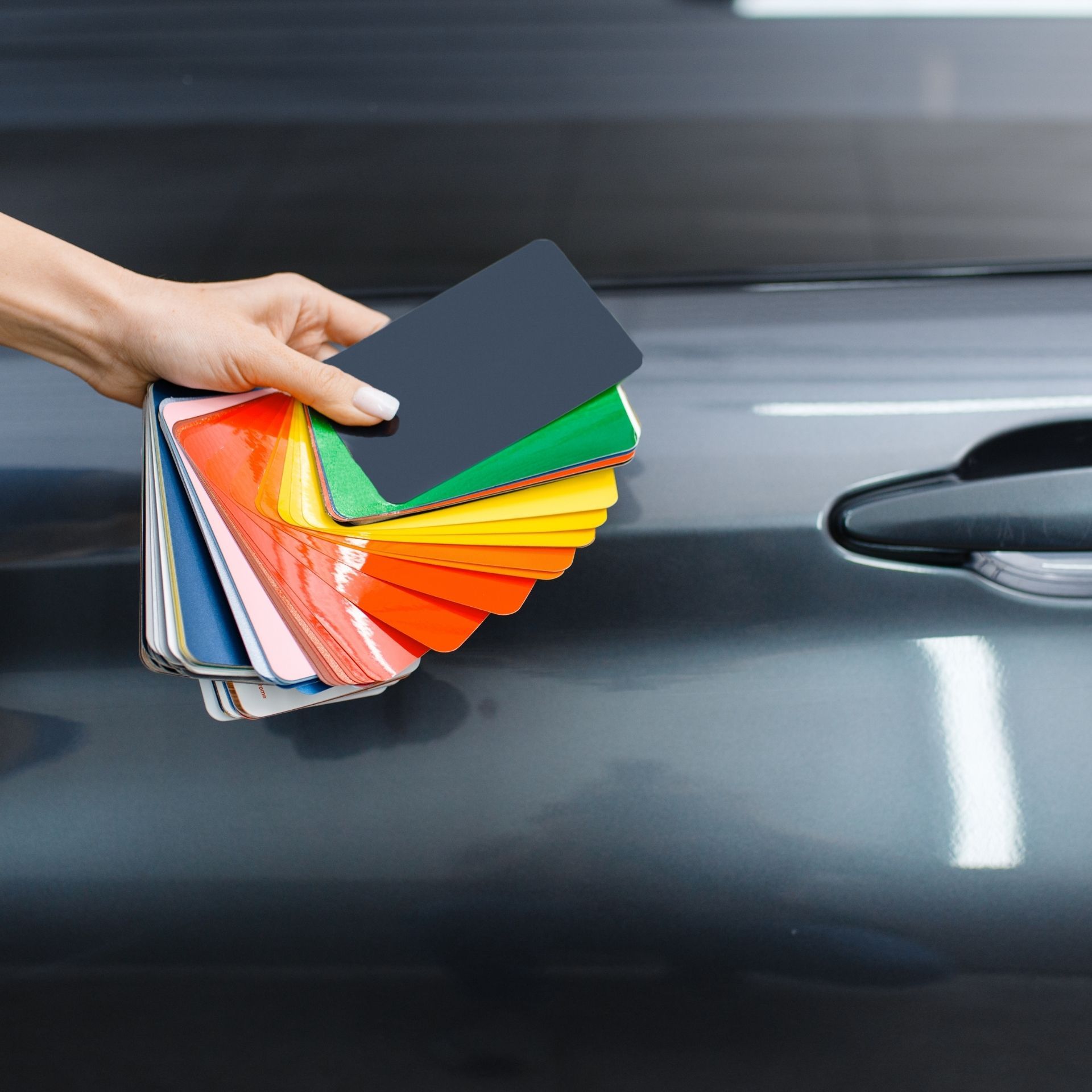 Hand holding a fan of colorful paint swatches against a dark car door