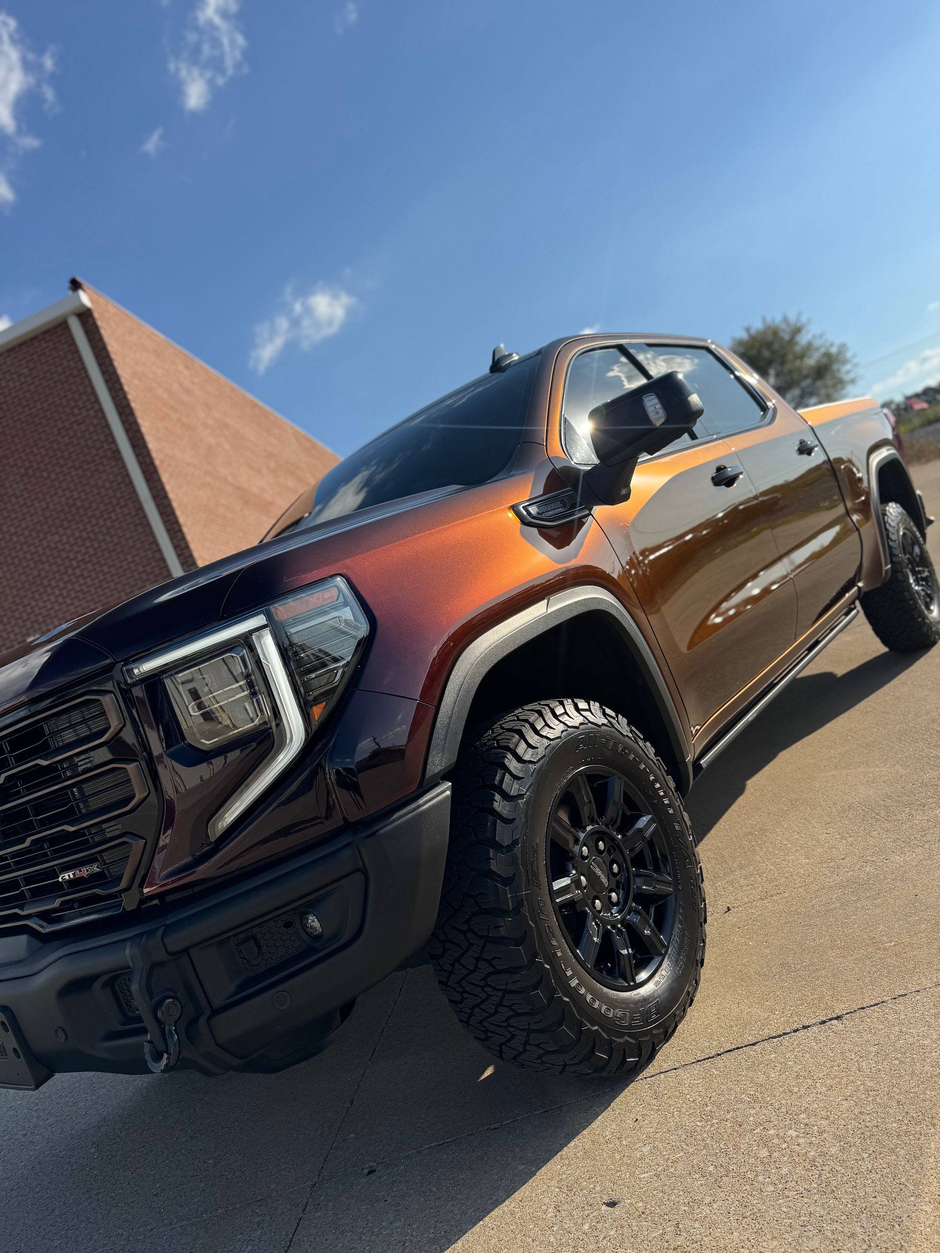 Black pickup truck with large off-road tires parked beside a brick building on a sunny day