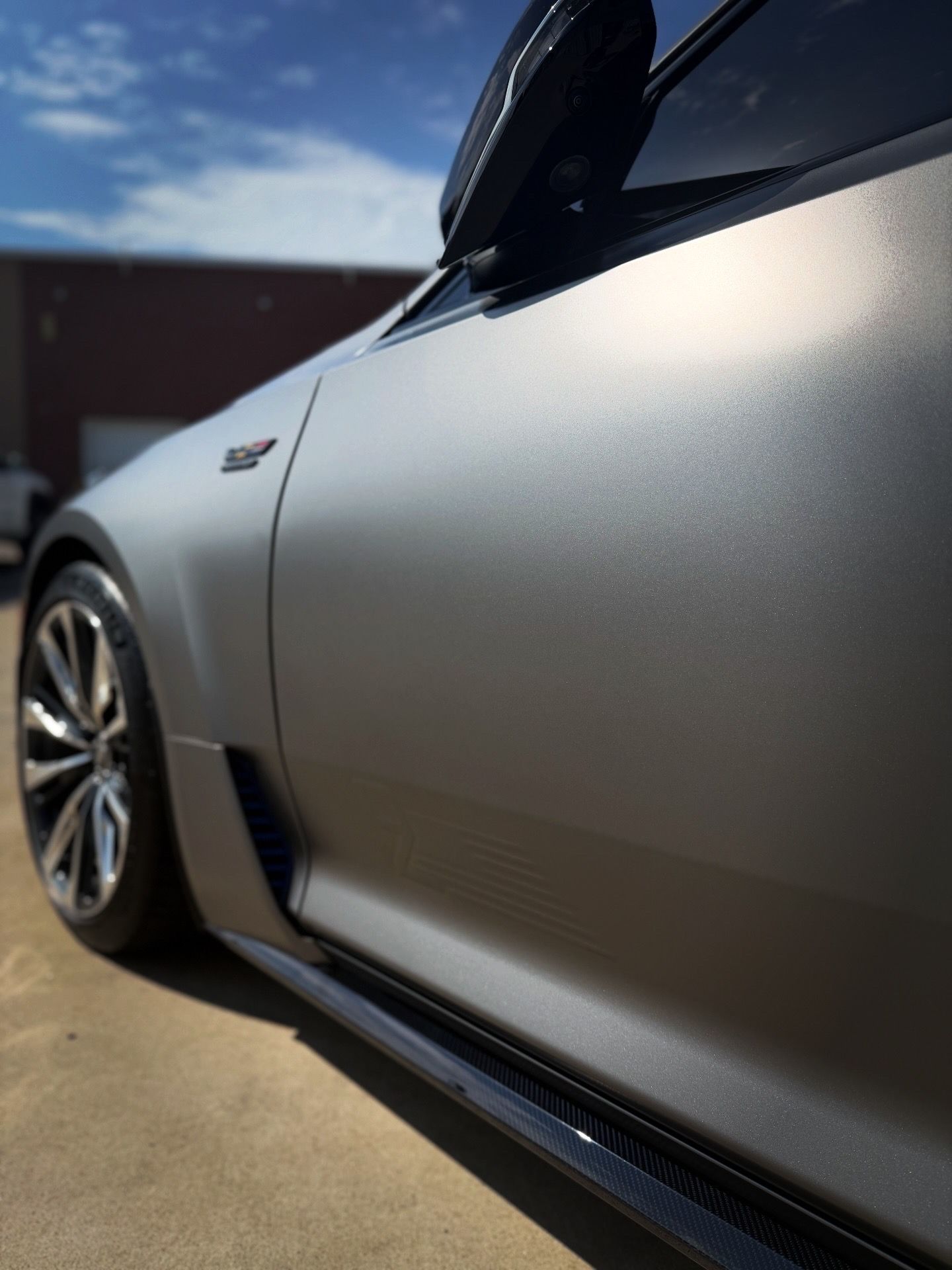 Silver car side panel parked outdoors in sunlight, with a wheel and dark trim visible.