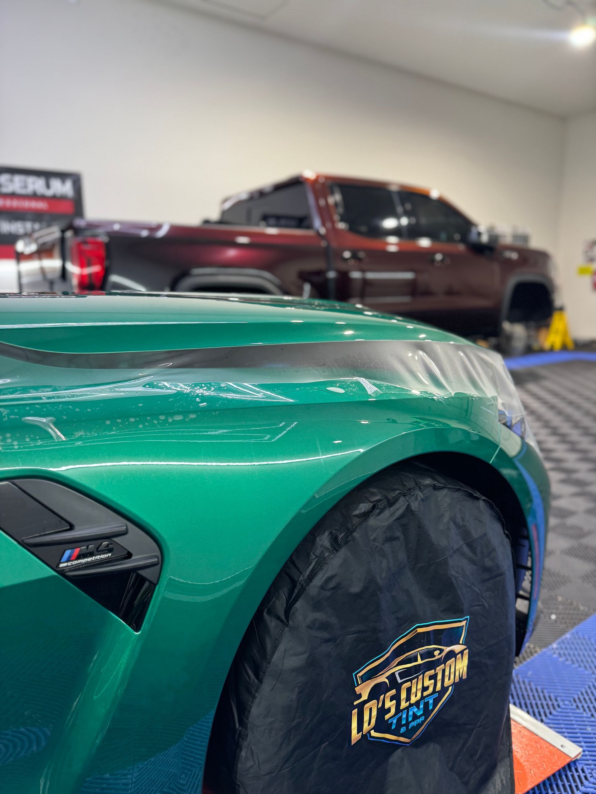 Green sports car in a garage, with a maroon pickup truck blurred in the background.