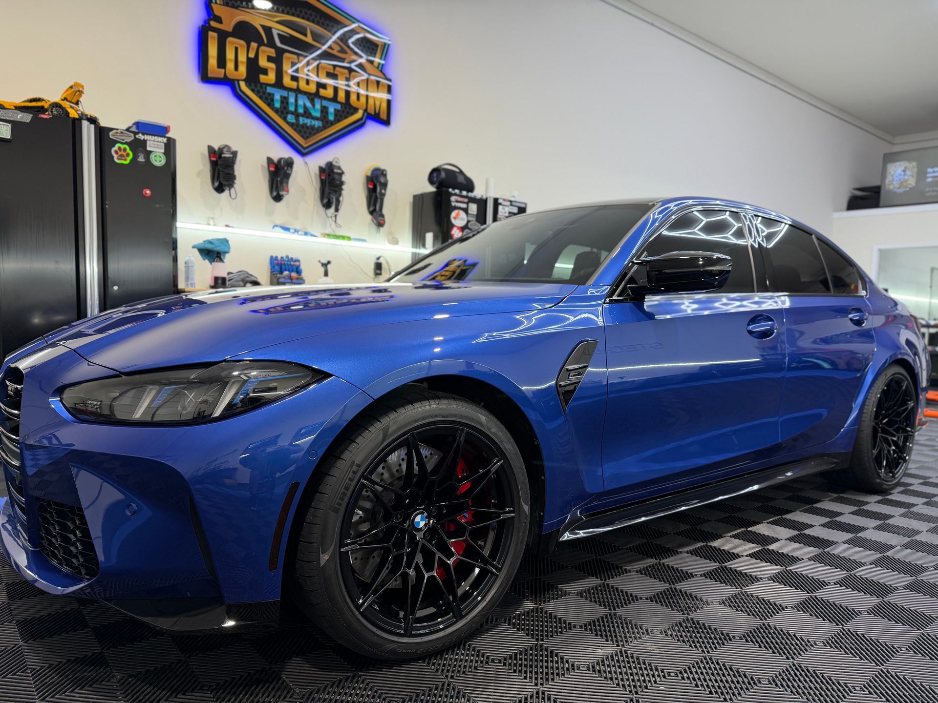 Blue BMW sedan in a detailing garage with black wheels and a patterned floor mat