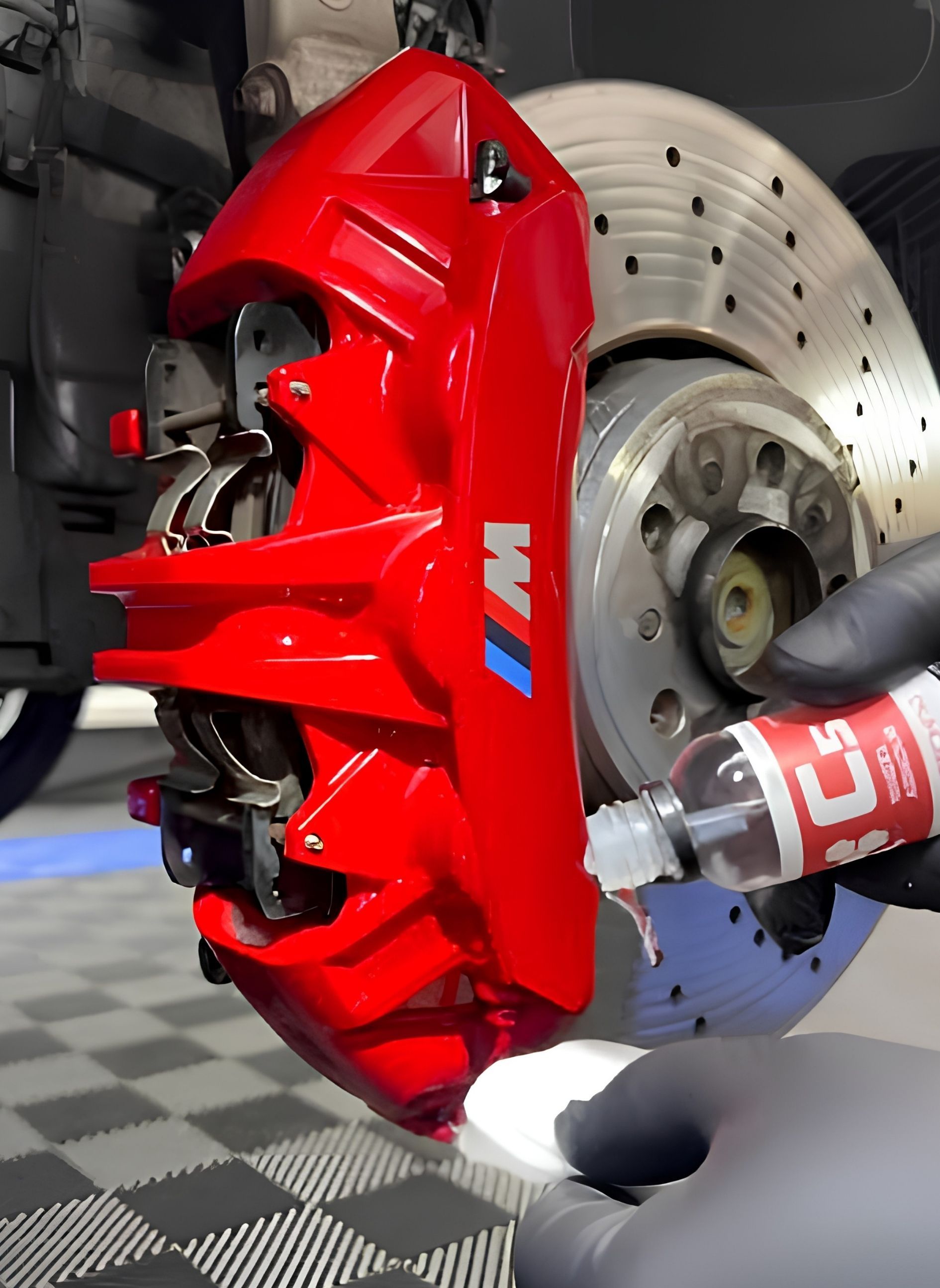 Red brake caliper being installed on a car wheel with a drill in a workshop