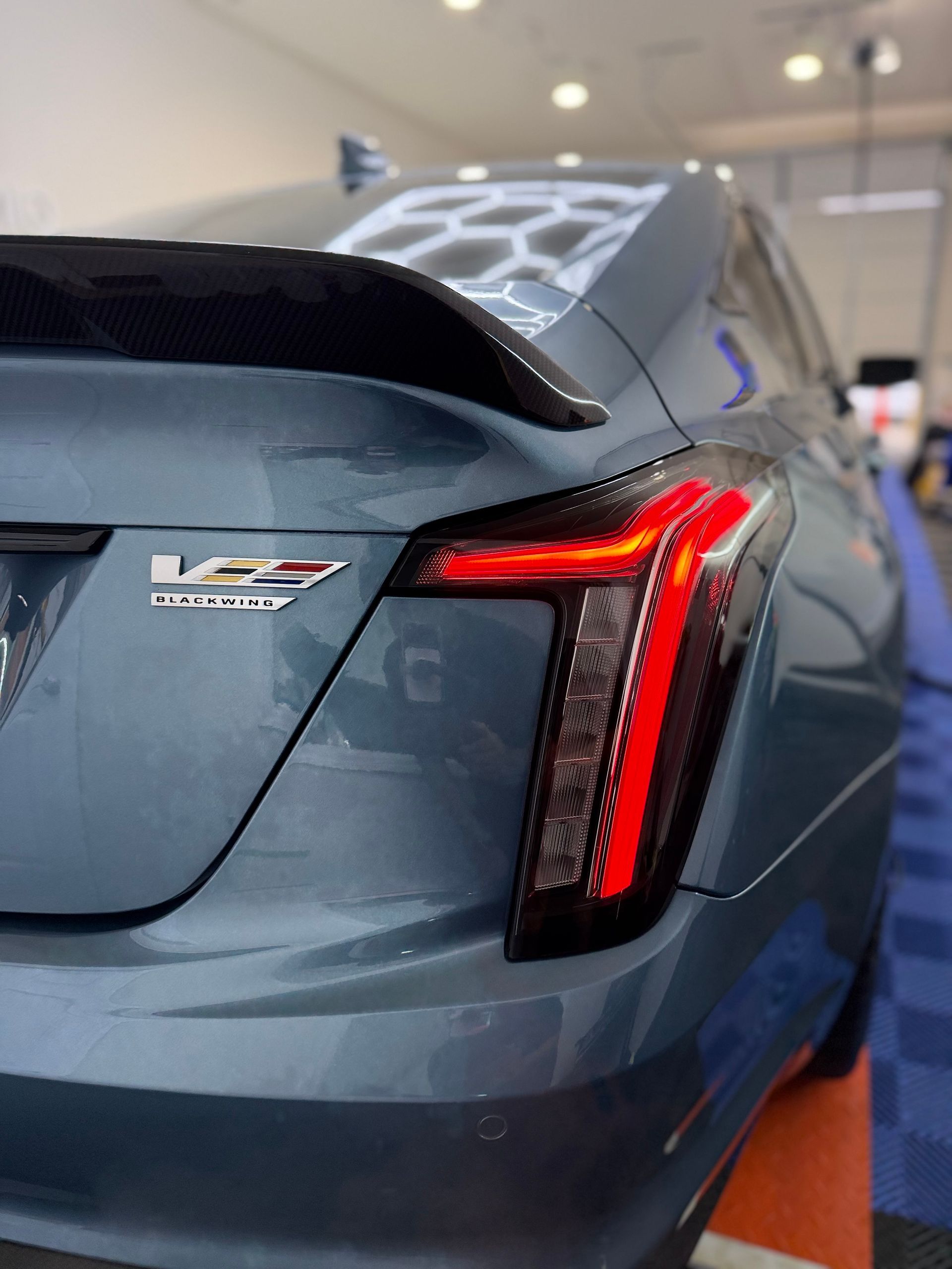 Close-up of a gray sports car’s rear with illuminated red taillight in an indoor showroom