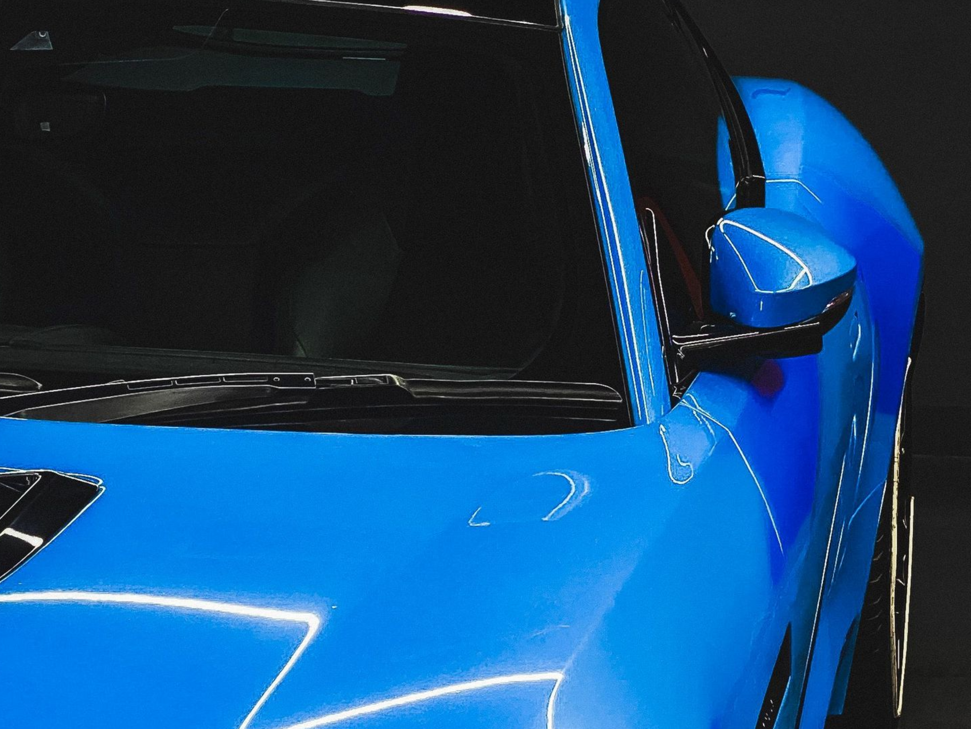Close-up of a blue sports car’s front hood, windshield, and side mirror
