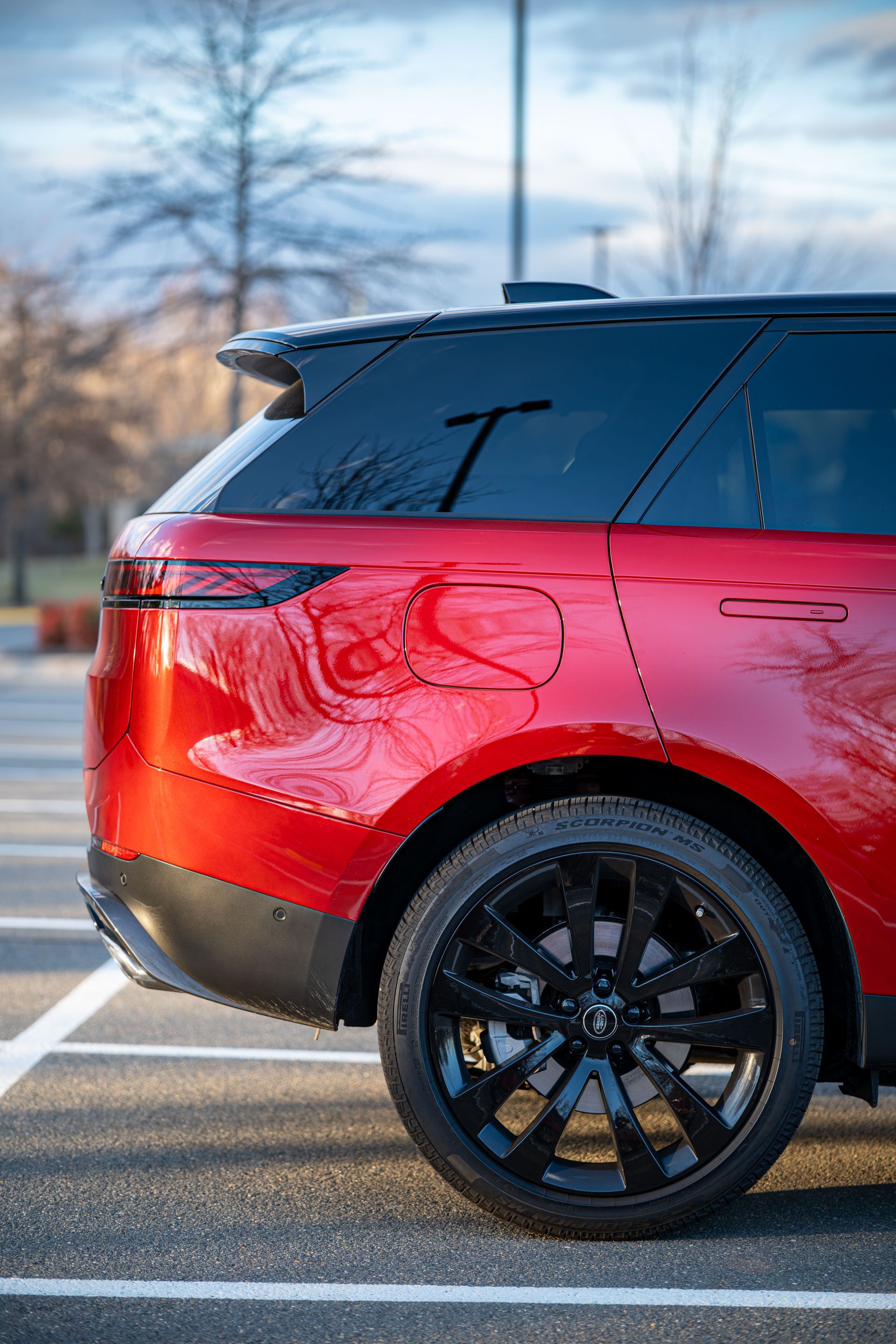 Rear side of a red SUV with black roof and wheels, parked outdoors in a snowy lot.