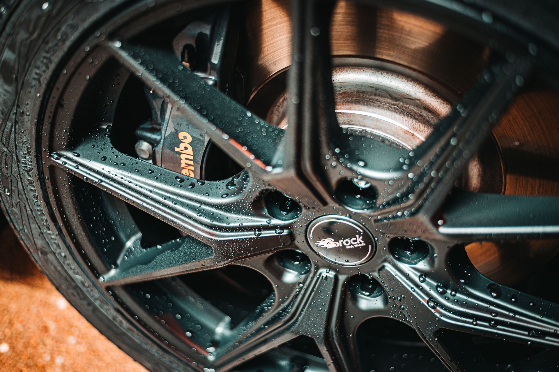 Close-up of a black alloy car wheel with water droplets and a visible brake caliper