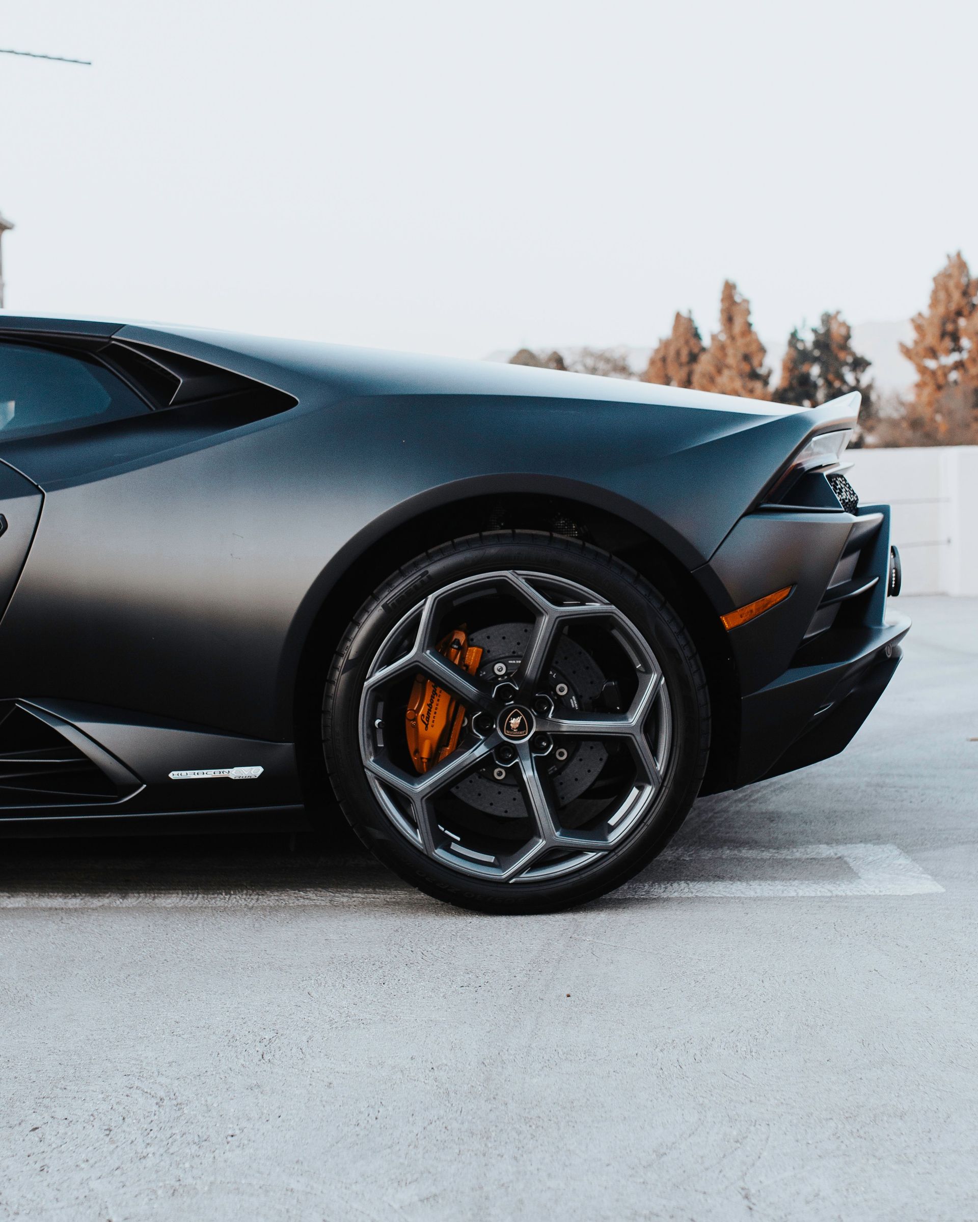 Front side of a dark gray sports car with black wheels parked on a snowy road.