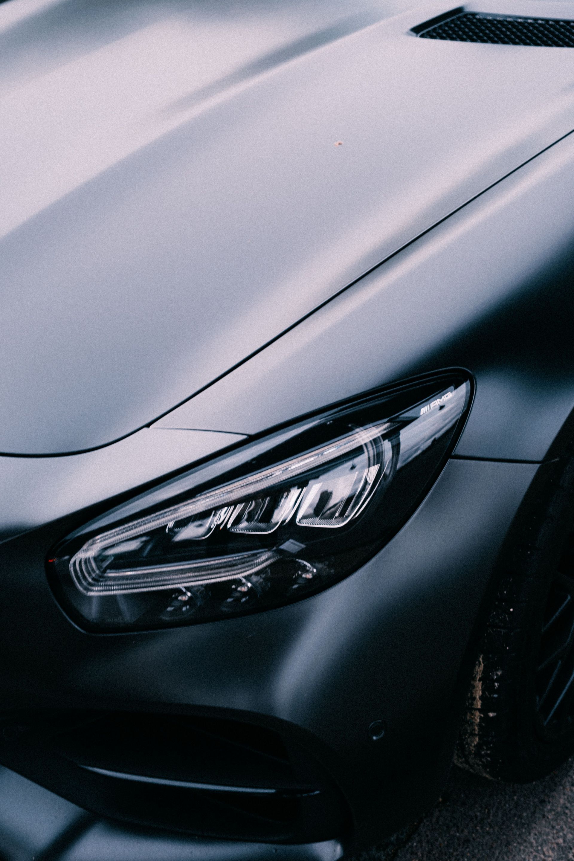 Close-up of a gray car’s front headlight and hood