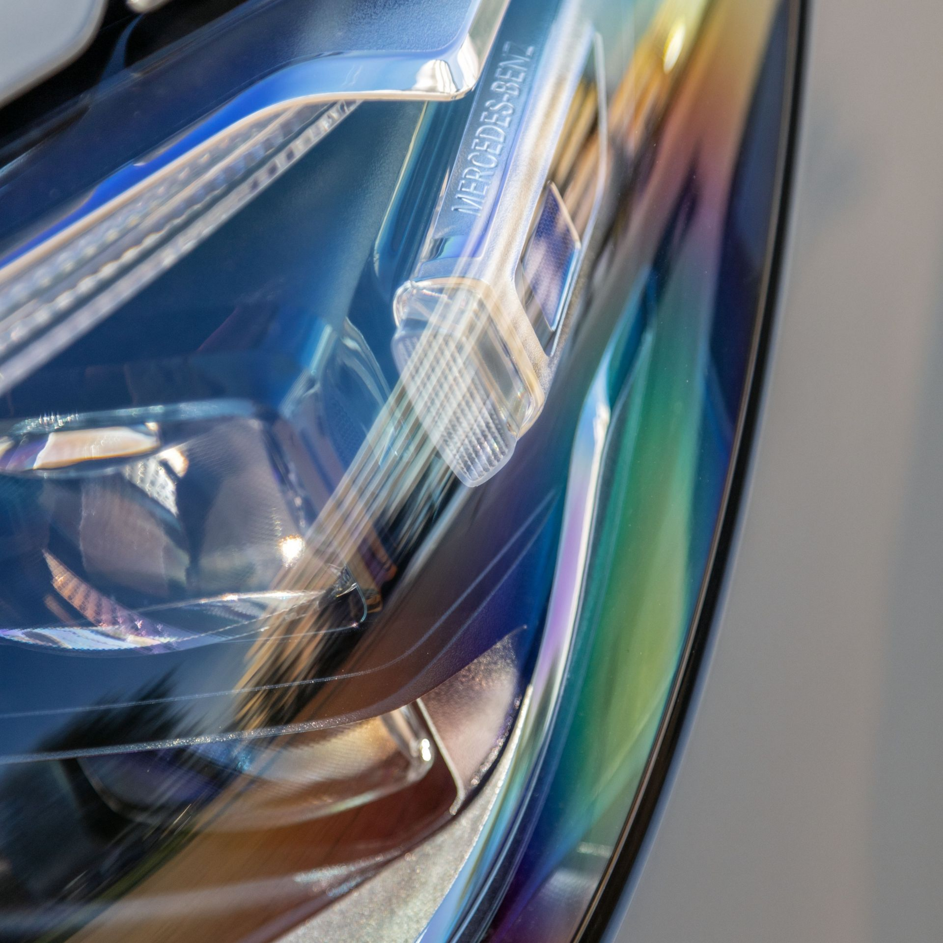 Close-up of a glossy car headlight with blue and rainbow reflections