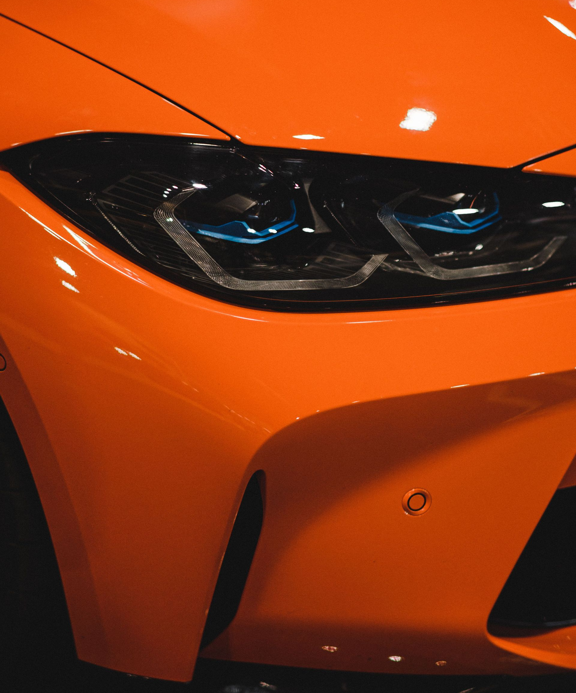 Close-up of a silver car headlight covered in raindrops and reflections