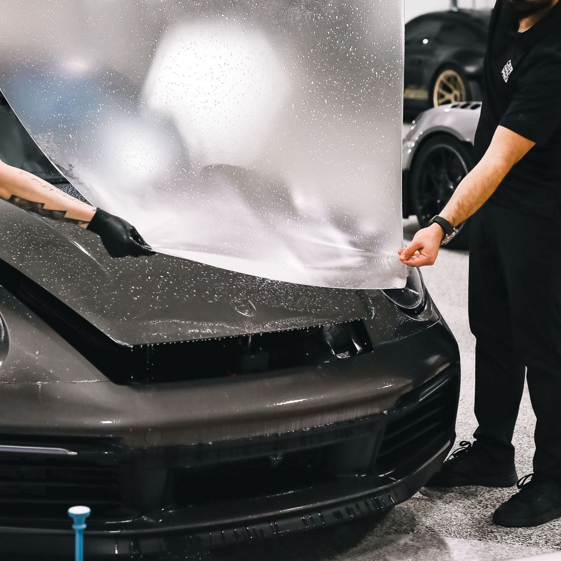 Two people washing a black sports car with a soapy foam sheet