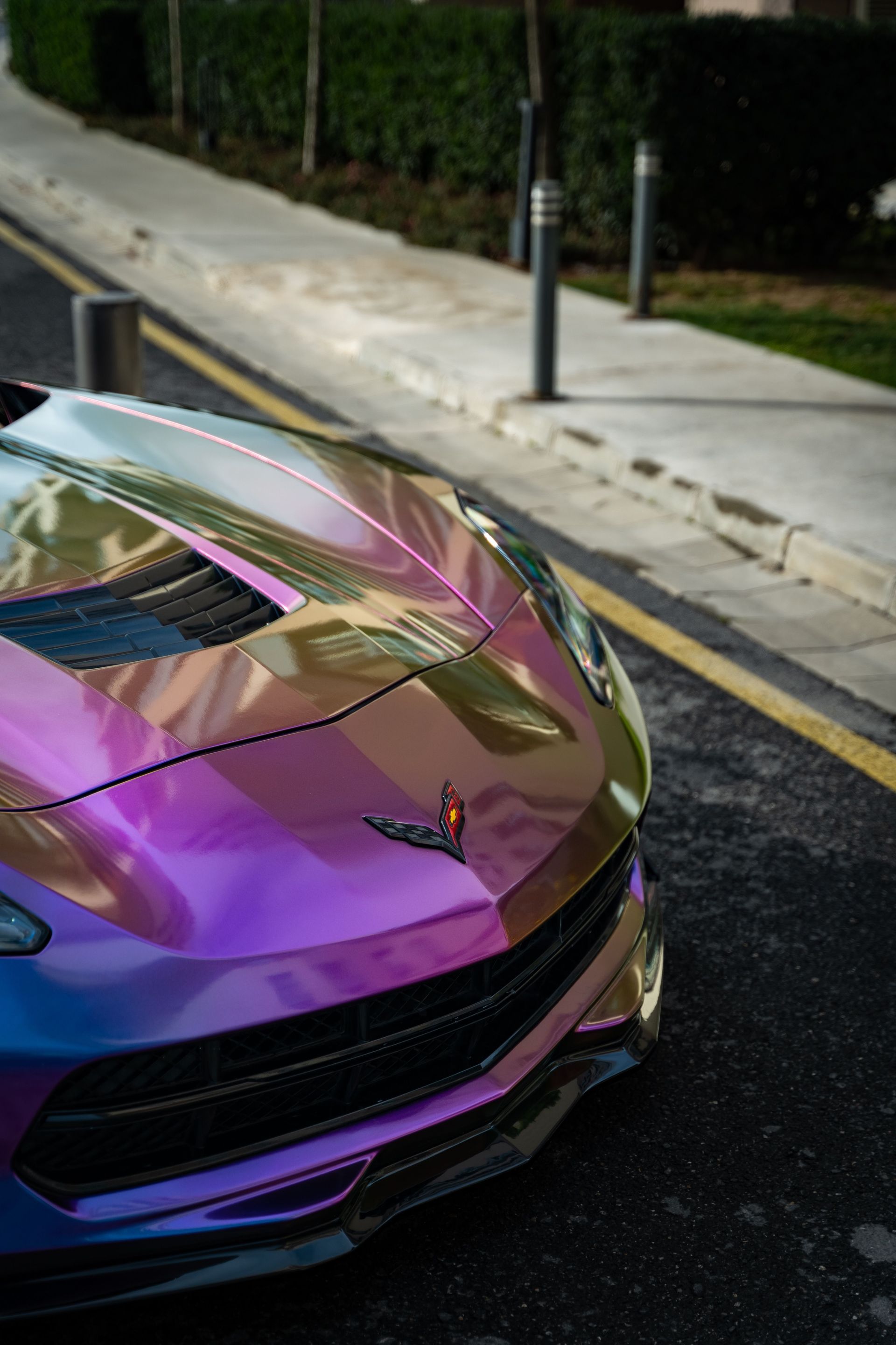 Purple sports car parked on a curb beside a sidewalk and hedge-lined street