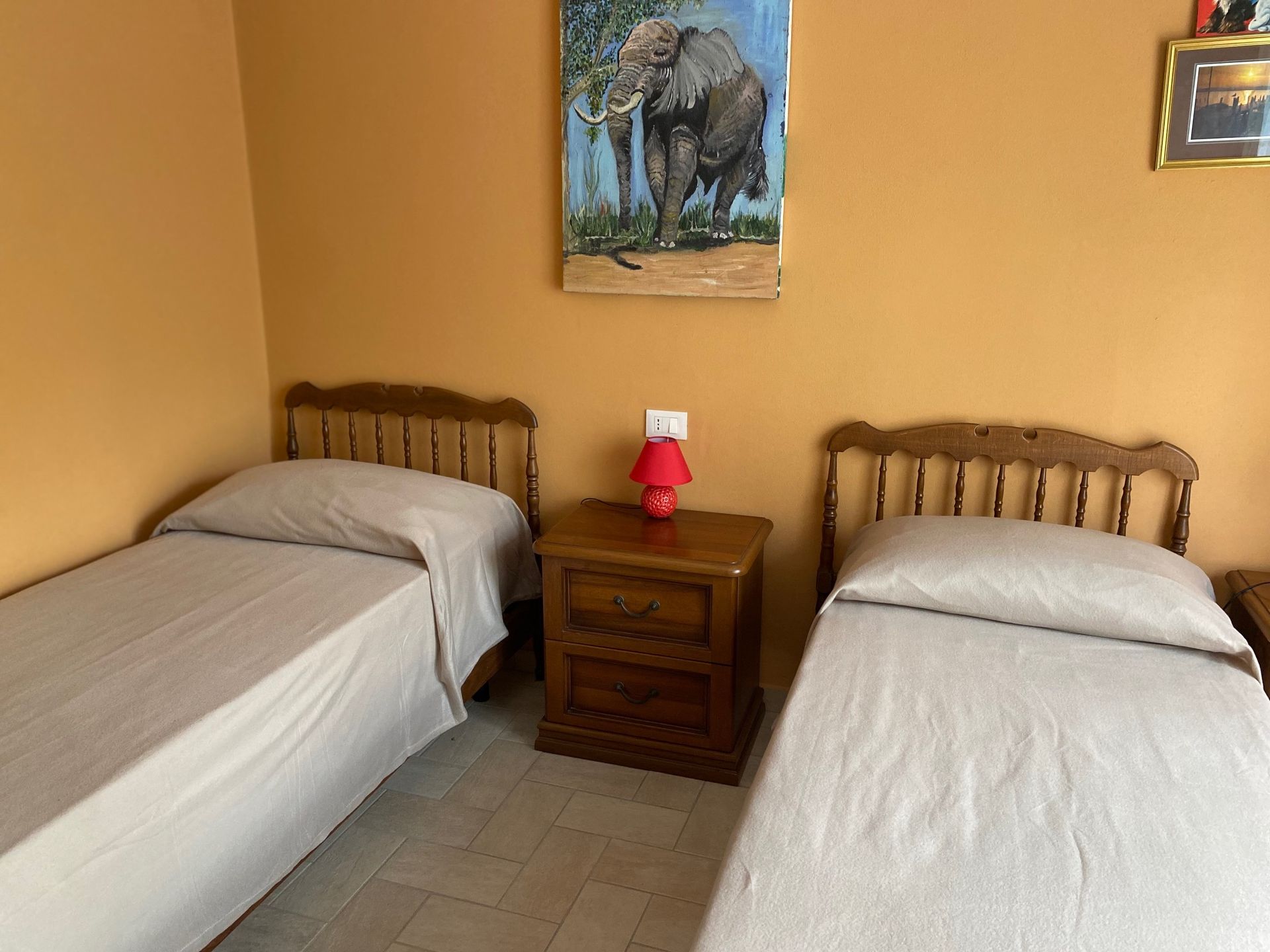 A room with two beds and a painting of an elephant on the wall.