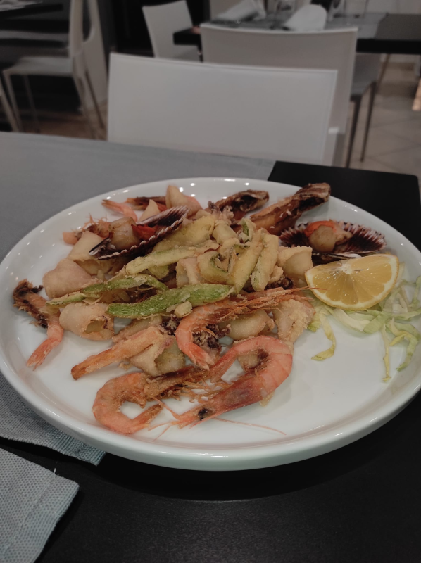 Piatto di gamberi grigliati con verdure e uno spicchio di limone su un tavolo di ristorante.
