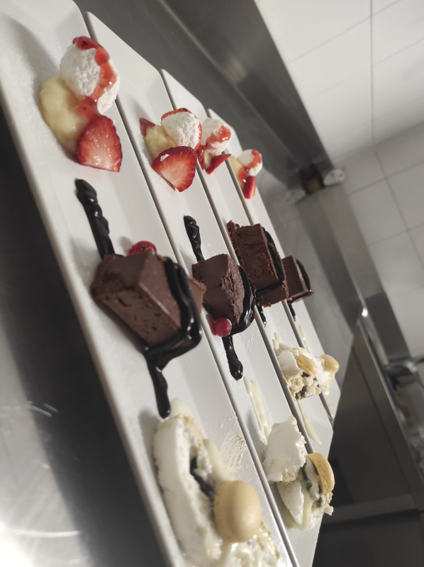 In una cucina, i dessert sono disposti su vassoi bianchi e infilzati su spiedini con pezzi ricoperti di cioccolato, fragole e panna.