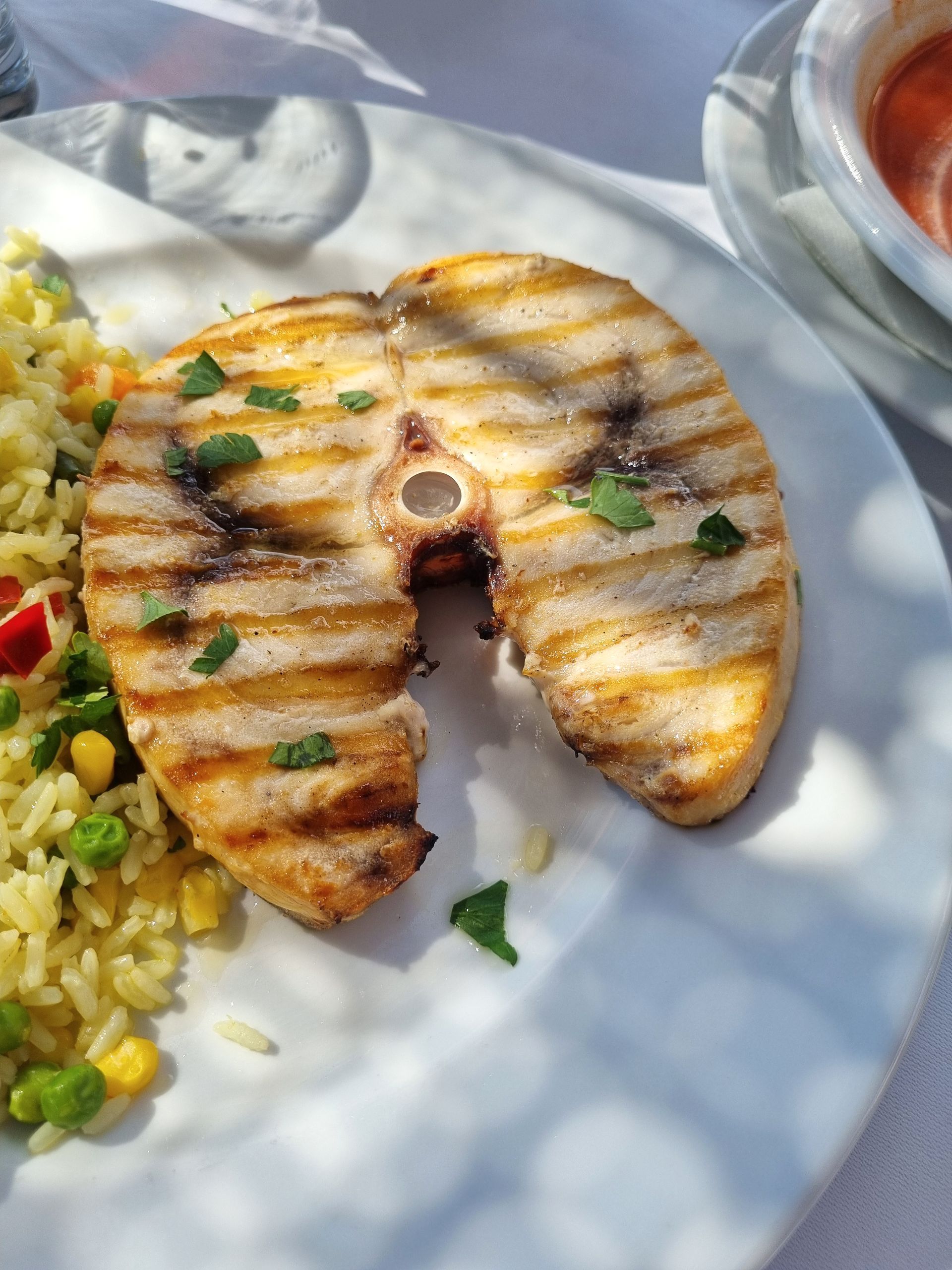 Filetto di pesce grigliato con riso e verdure su un piatto bianco, con una ciotolina di salsa a lato.
