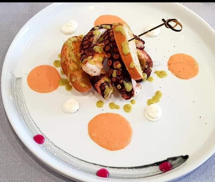 Dessert gourmet impiattato con salsa all'arancia, ciuffi di panna e frutti di bosco su un piatto bianco.