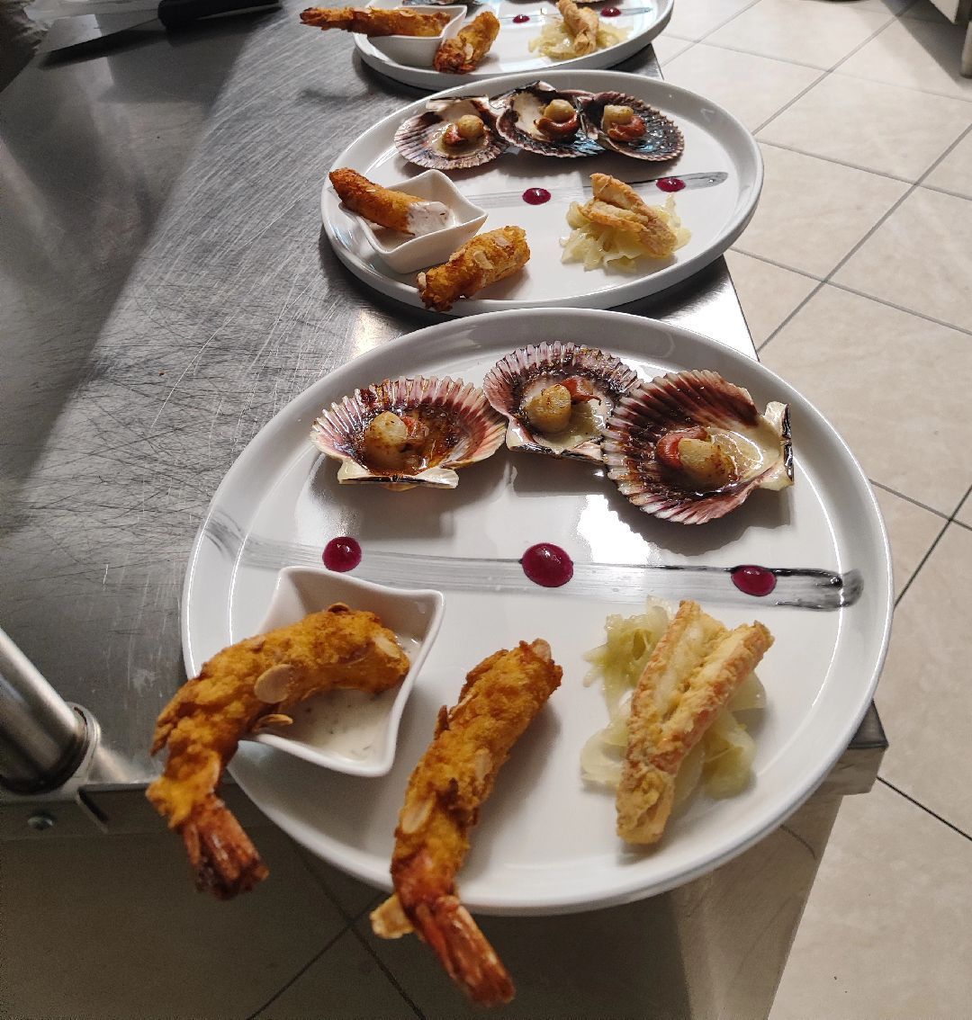 Su un tavolo piastrellato sono disposti piatti di antipasti assortiti a base di frutti di mare, tra cui gamberi, capesante e spiedini con salsa.