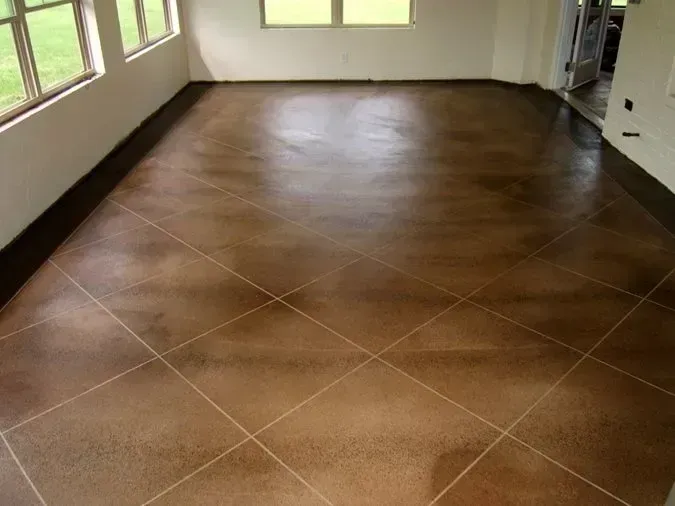 Empty room with brown tiled floor, white walls, and large windows letting in natural light