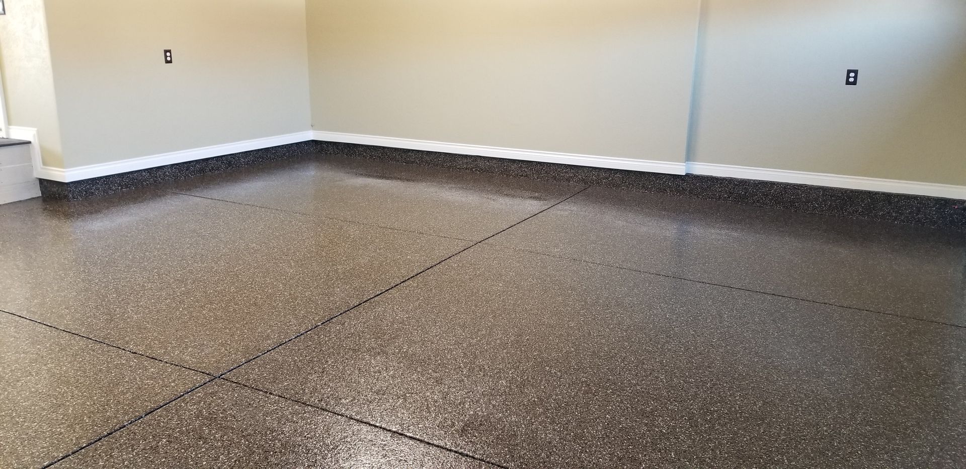 Empty speckled epoxy floor in a room with white walls and black baseboards
