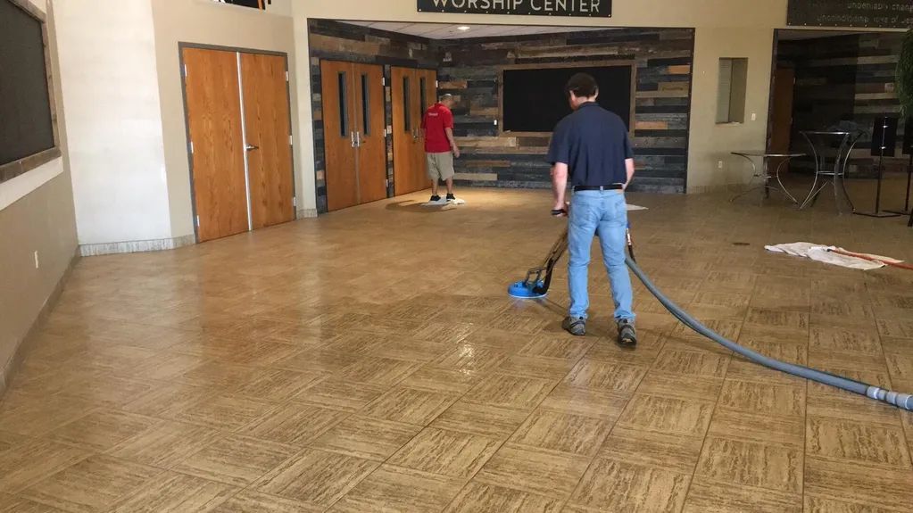Two people cleaning a flooded lobby floor with a wet vacuum and hose