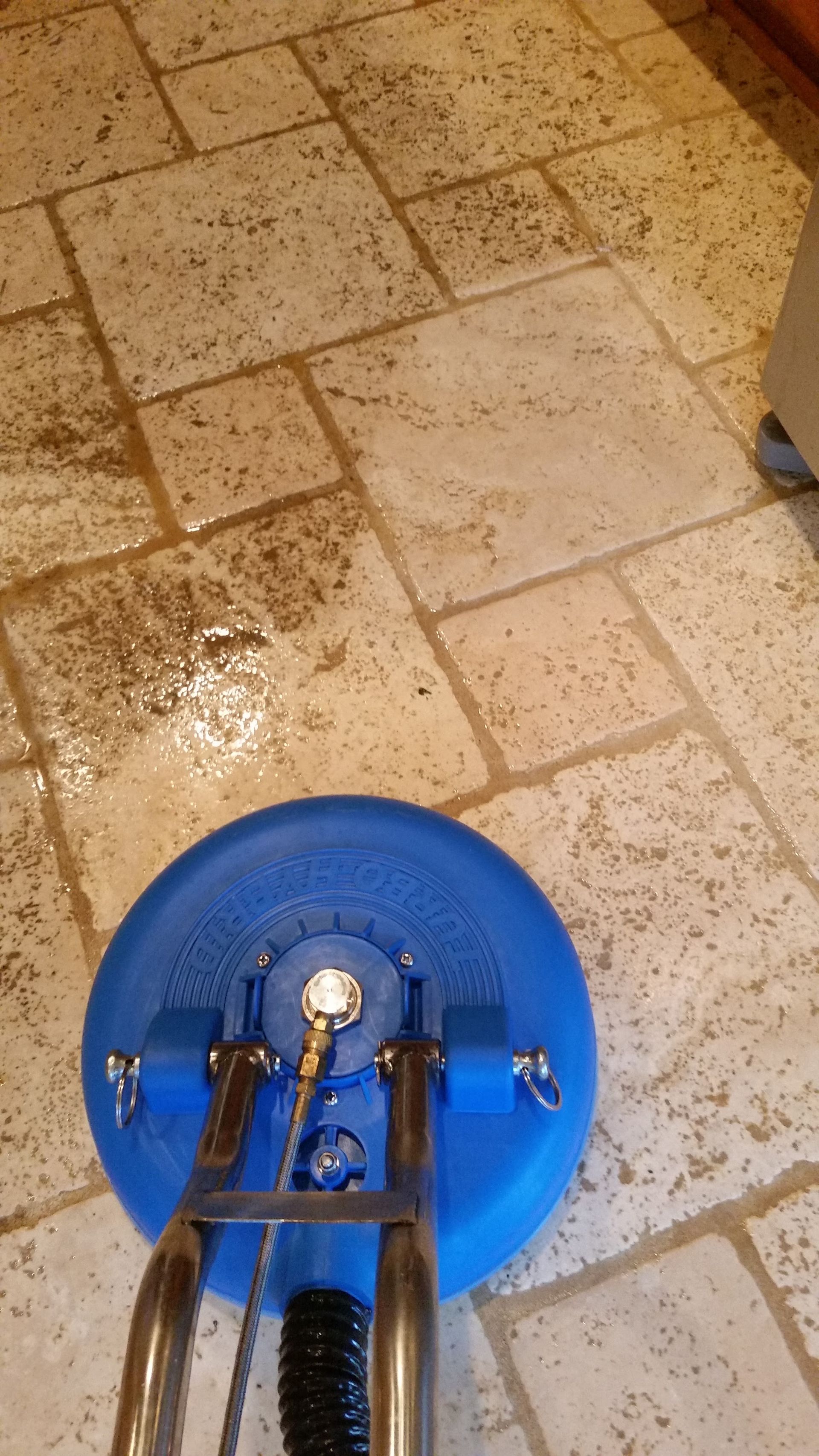 Blue floor scrubber cleaning a beige tiled floor with wet, soapy patches