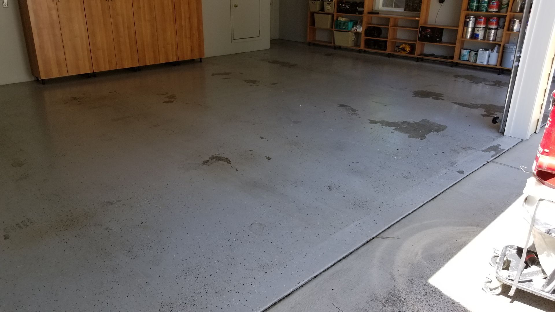 Empty concrete garage floor with scattered stains and a wooden wall at the back.