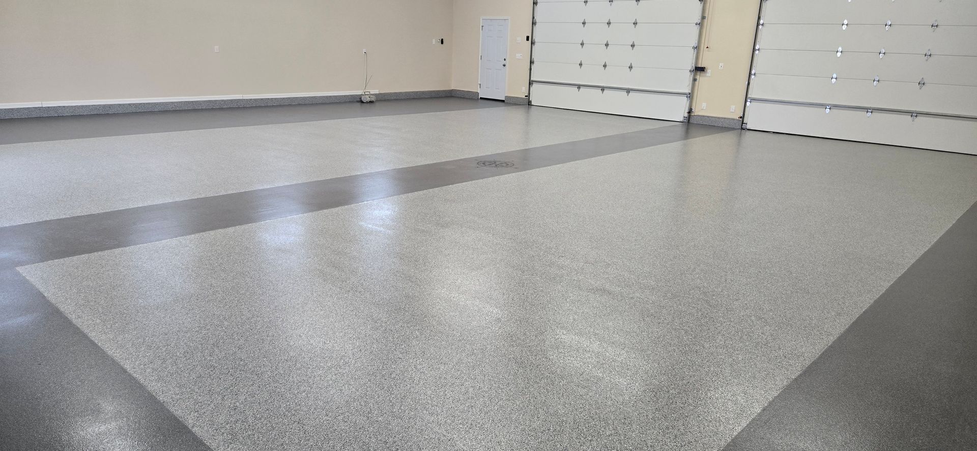 Empty garage with a speckled gray floor and white garage doors in the background