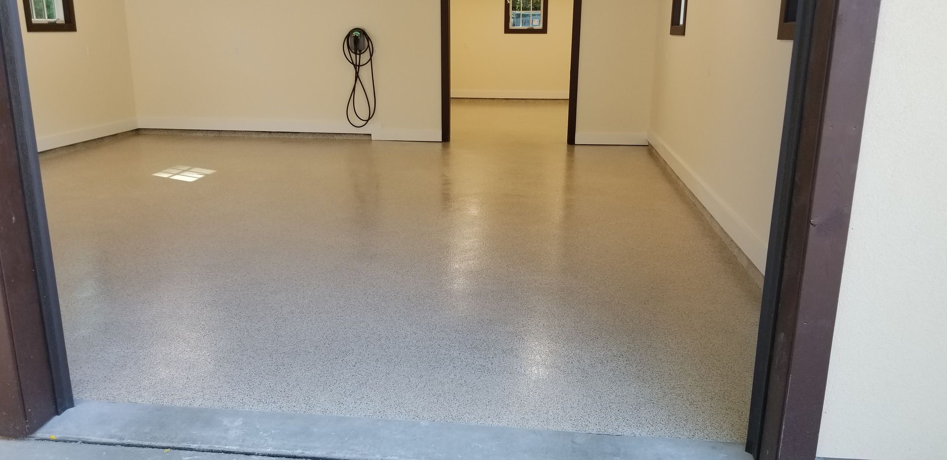Empty hallway with beige walls, gray speckled floor, and doorways on both sides