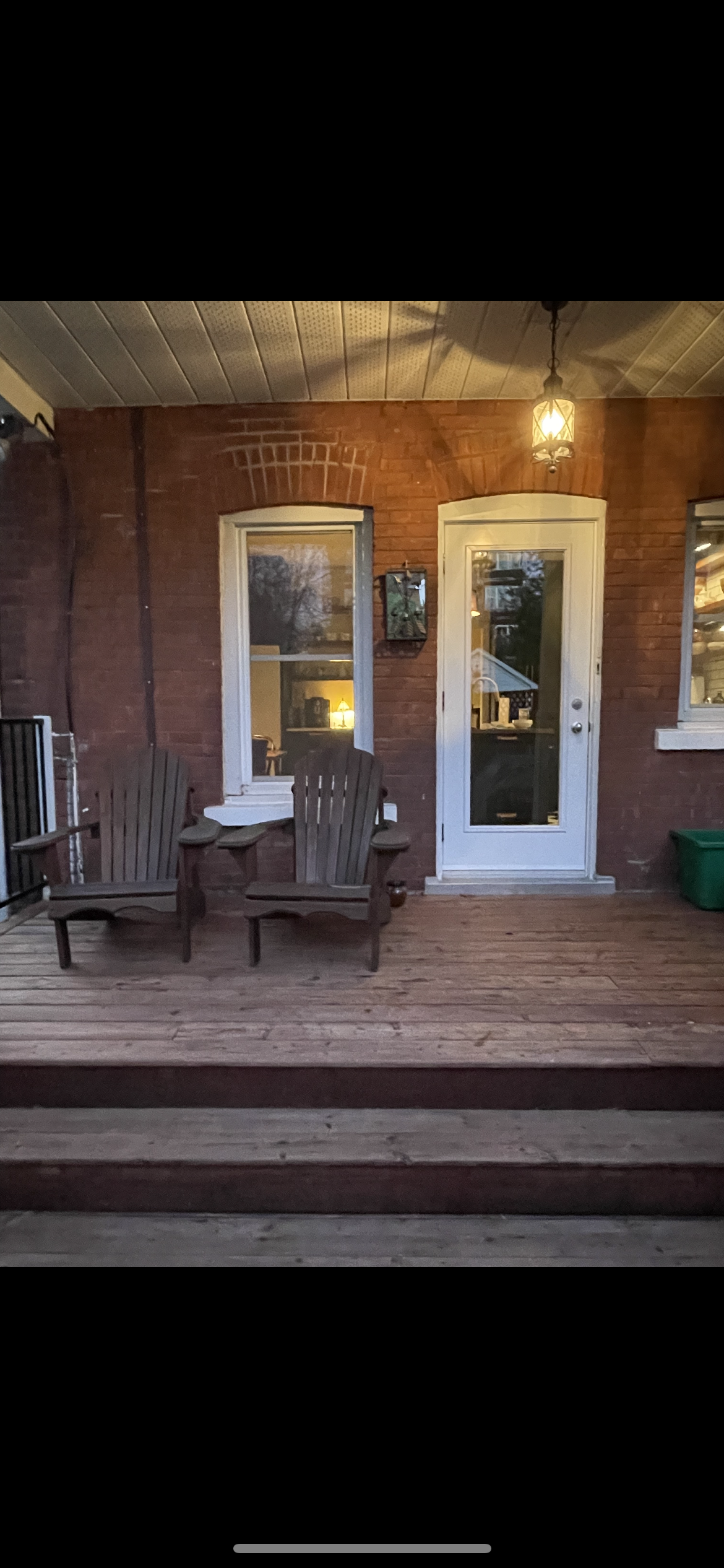 Une terrasse en bois avec deux chaises et une table devant une maison en brique.