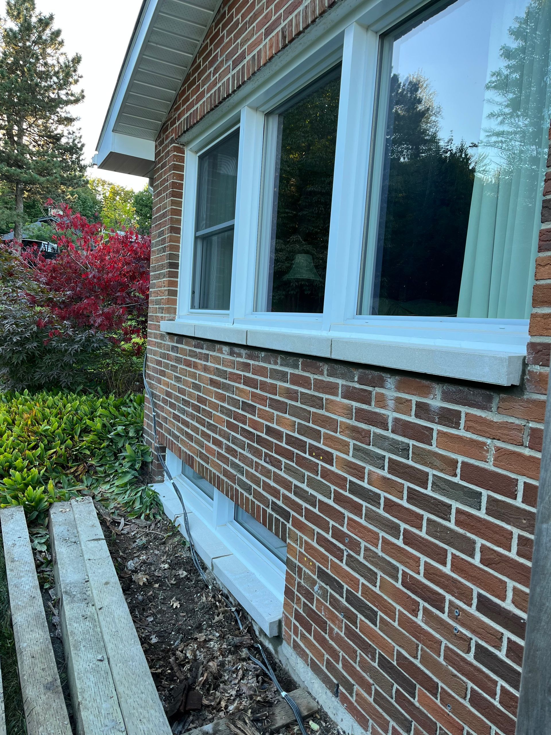 Une maison en brique avec des fenêtres blanches et un jardin devant.