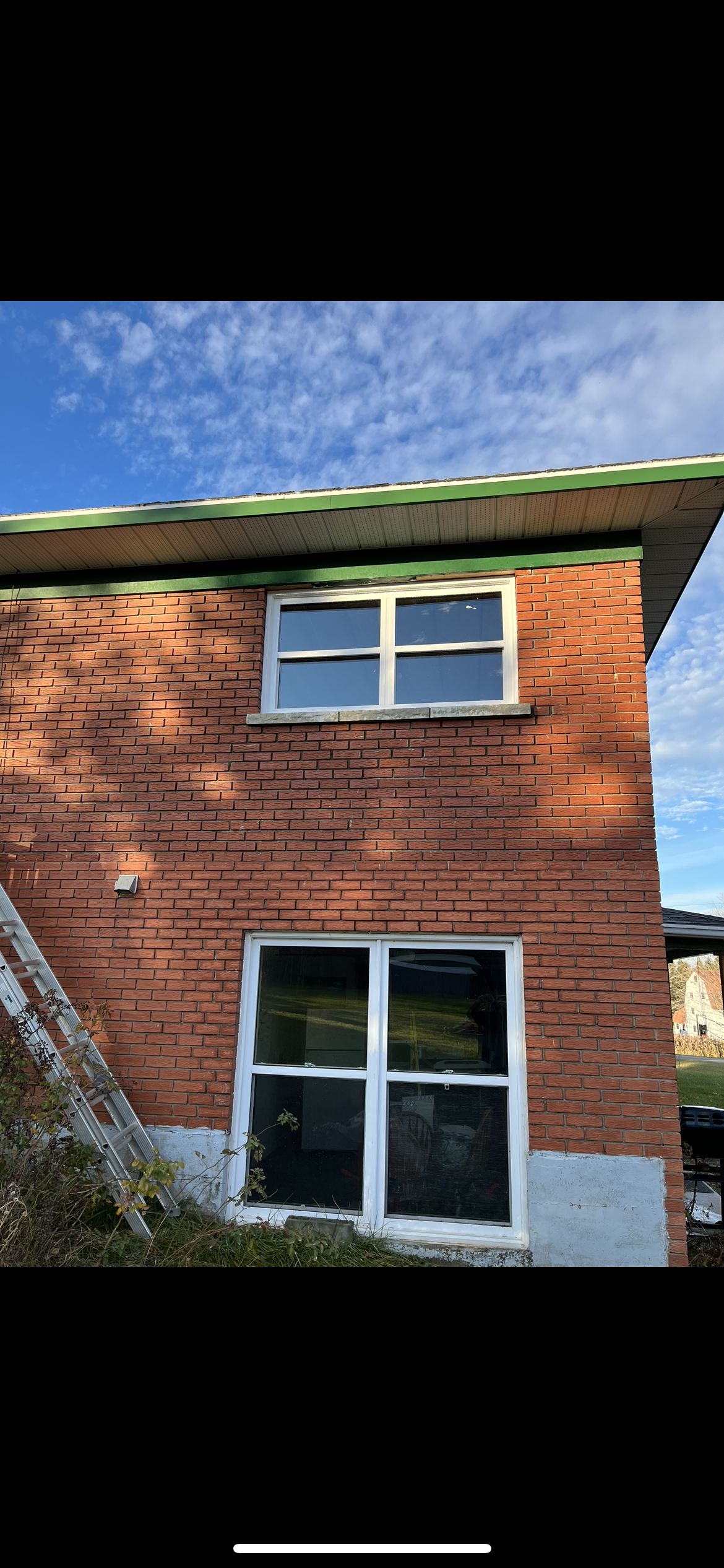 Une maison en brique avec une fenêtre blanche et un toit vert.