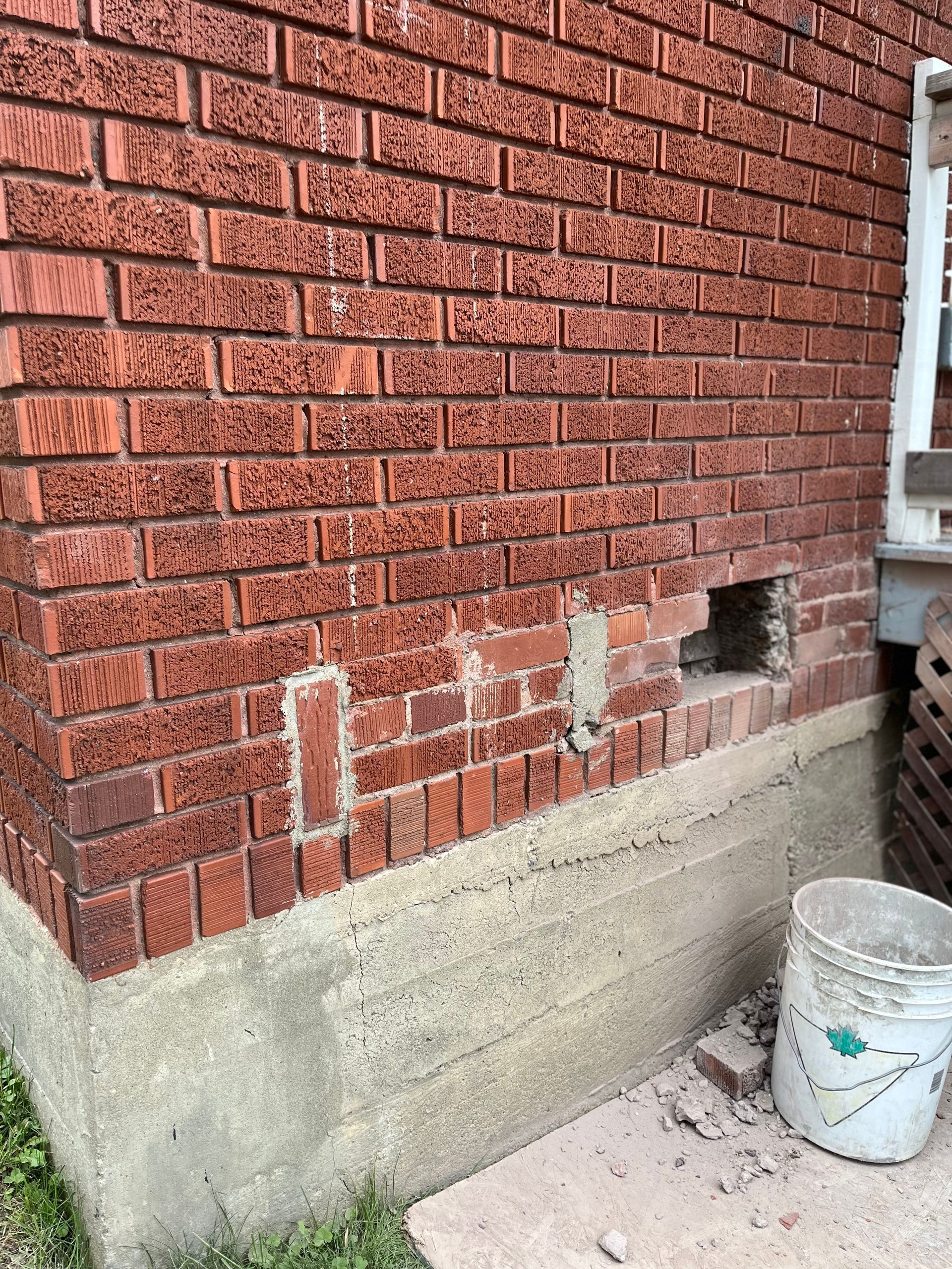 Un mur de briques avec un trou et un seau à côté.