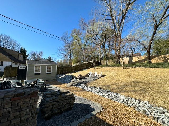 Backyard with stacked stone, a small shed, bare trees, and a rock-bordered path under a blue sky