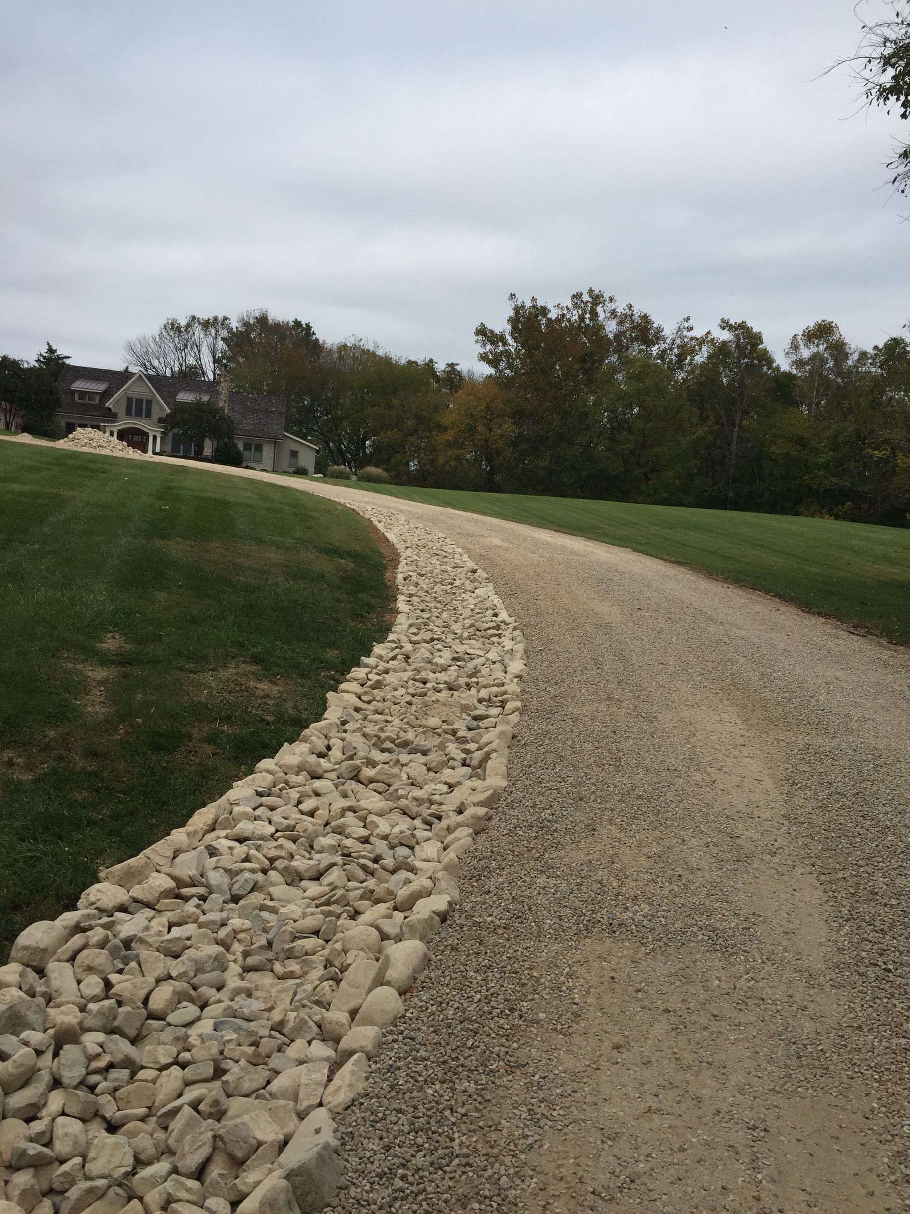 Curving gravel path with a stone border through a grassy park under a cloudy sky