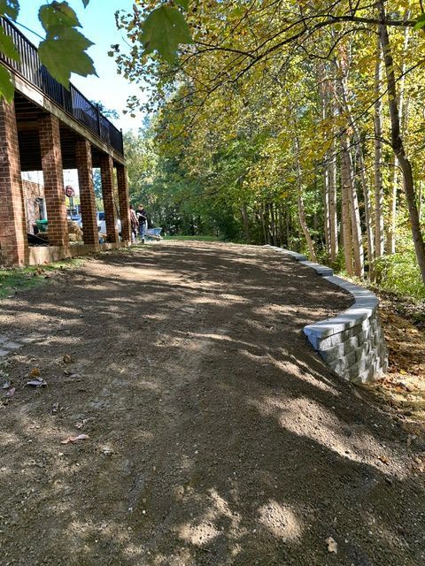Wooded dirt path beside a rustic pavilion, with sunlight and trees lining the trail