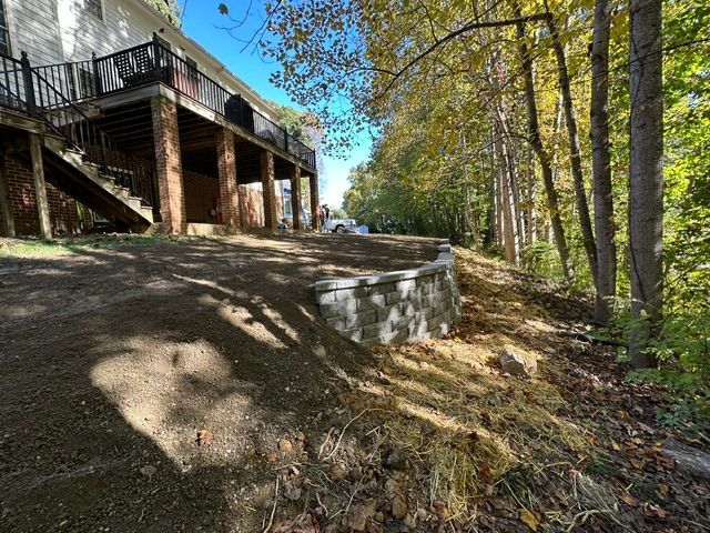 Wooded hillside beside a raised deck and stairway, with a concrete retaining wall in autumn light