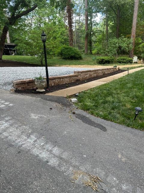Driveway beside a gravel path and low wooden border in a leafy backyard with lamp posts.