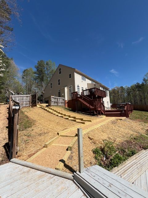House with red deck and stairs on a sloped yard under a clear blue sky