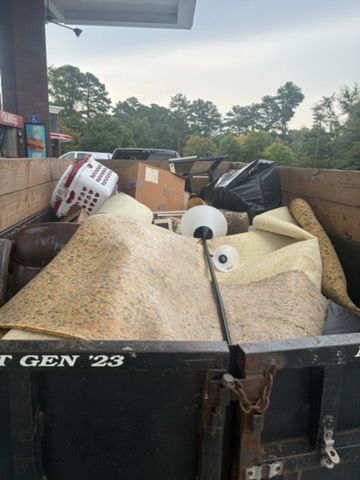 Dumpster filled with furniture, cardboard, and foam debris outdoors beside a building