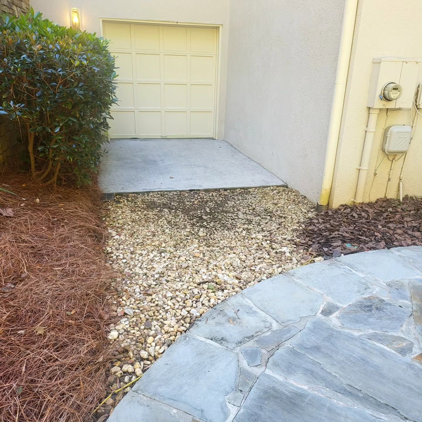 Curved stone walkway leading to a garage door beside bushes and utility meters