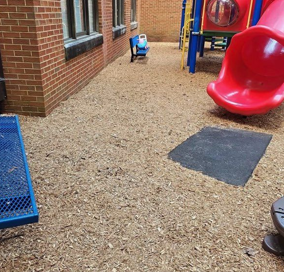 Playground with gravel surface, red slide, blue climbing equipment, and a small blue ride-on toy near a brick wall