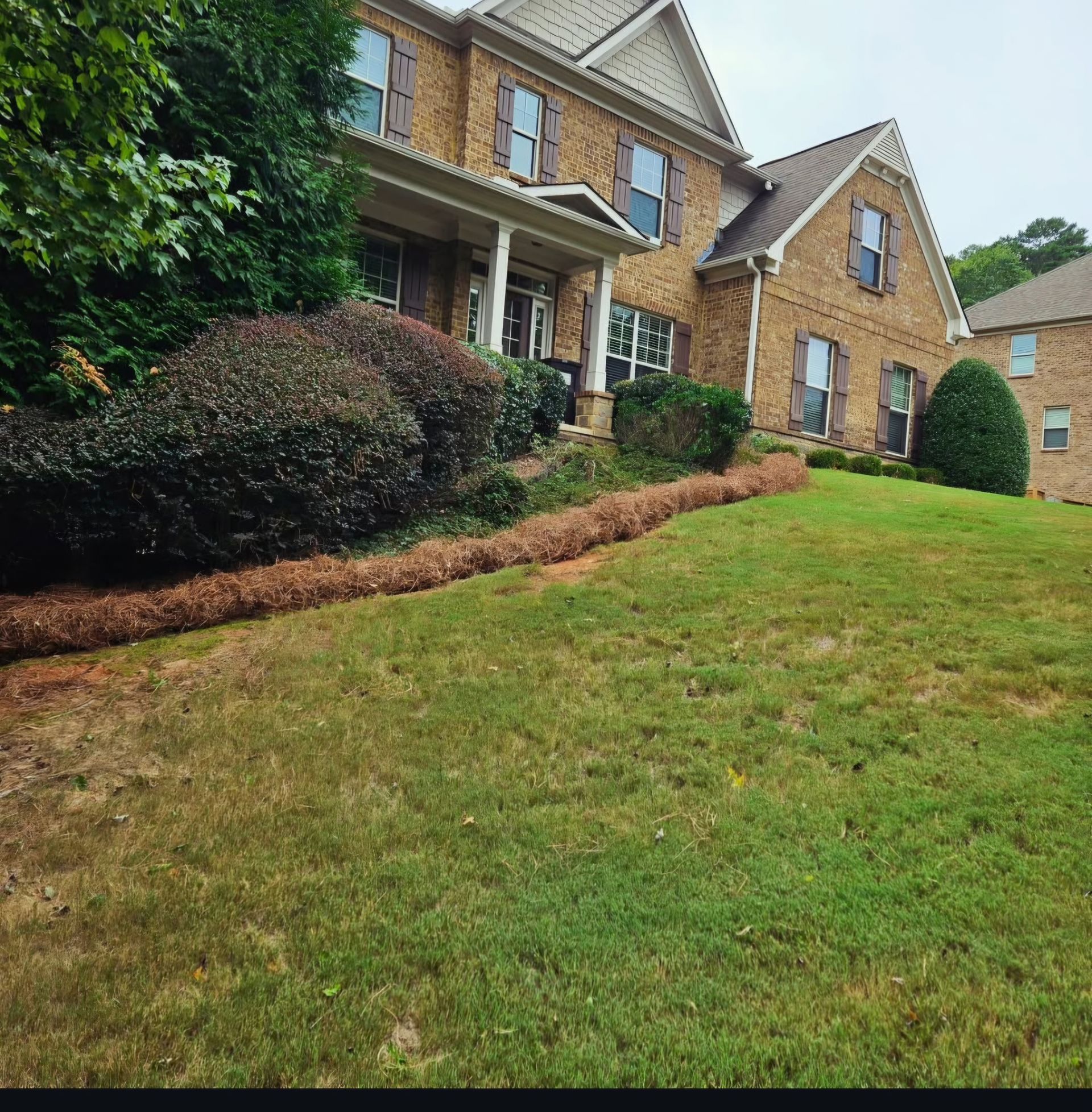 Brick suburban house with a covered porch, dormer windows, and a sloped green lawn