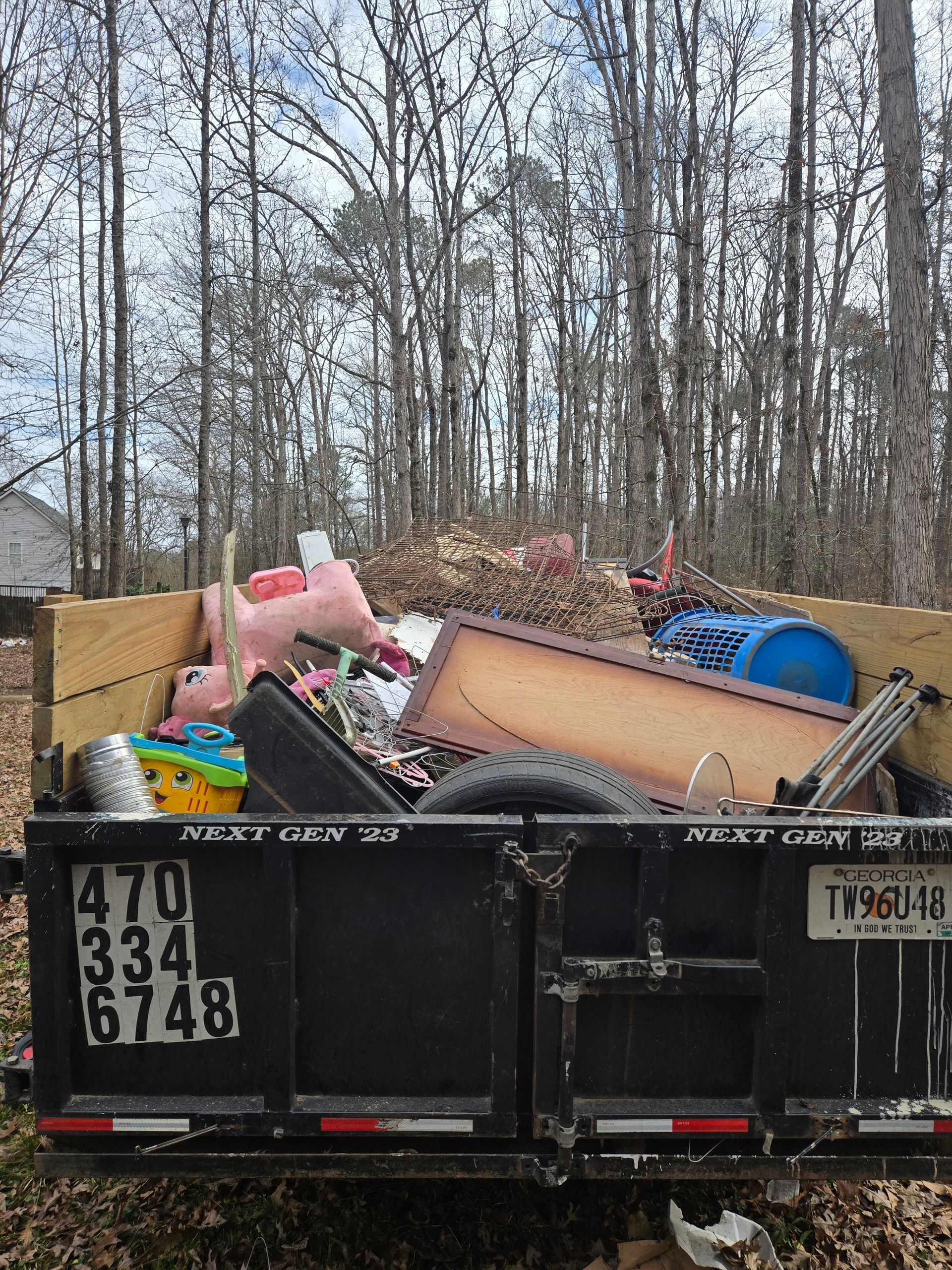 Overflowing black dumpster filled with discarded furniture and debris in a wooded area