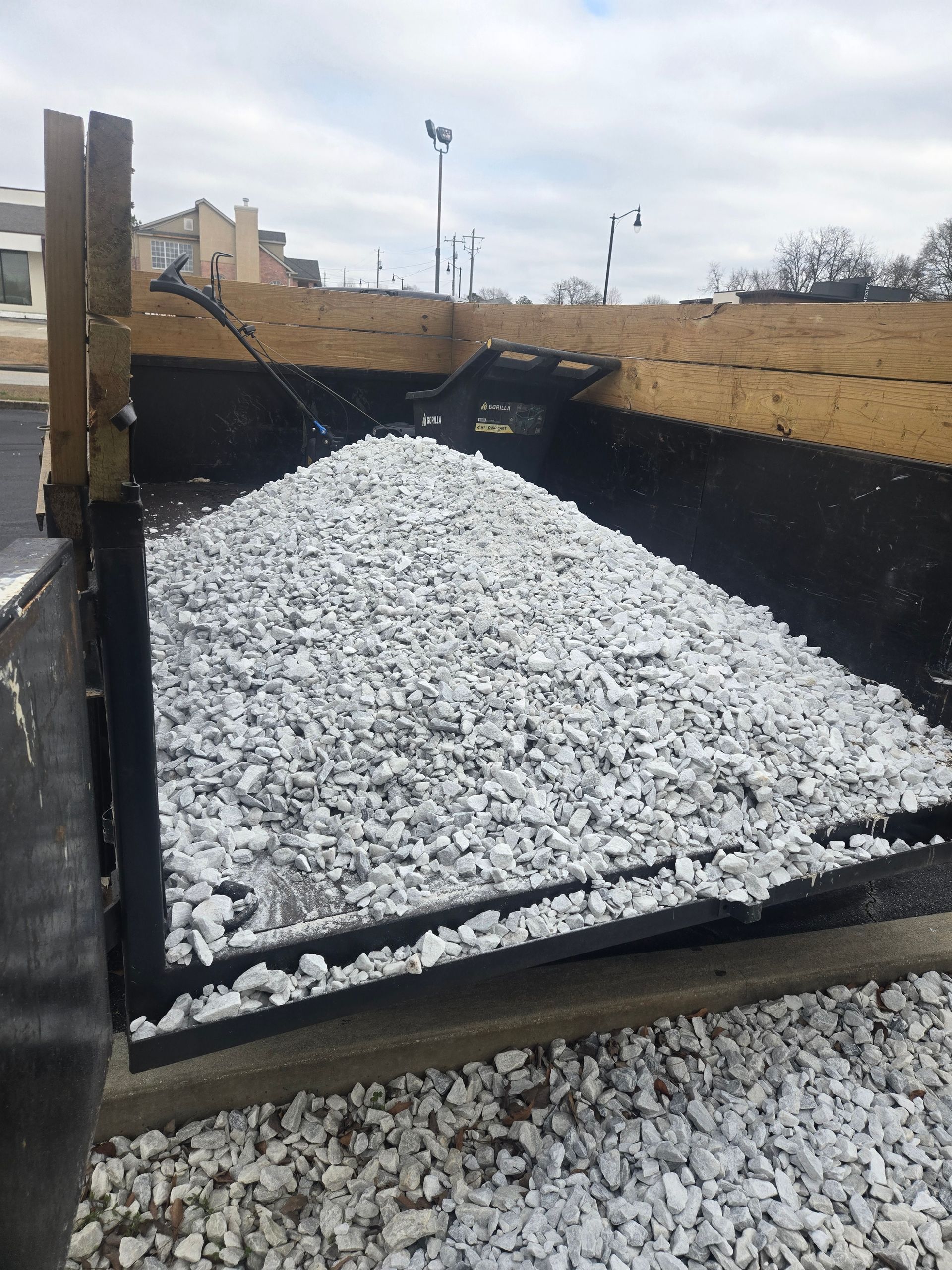 Truck bed filled with white gravel at a construction site with an excavator in the background