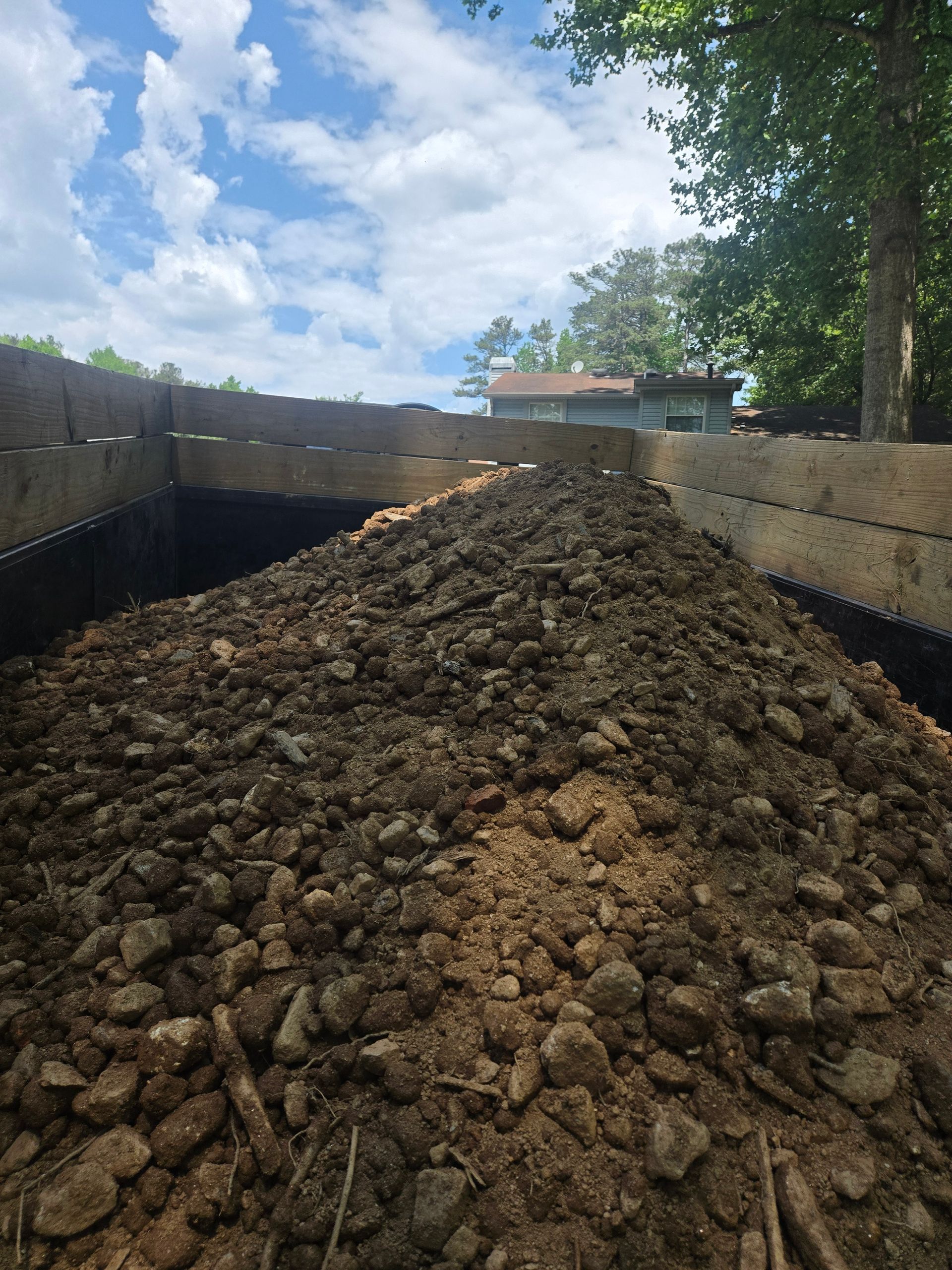 Large pile of soil in a metal-sided trailer outdoors under a partly cloudy sky